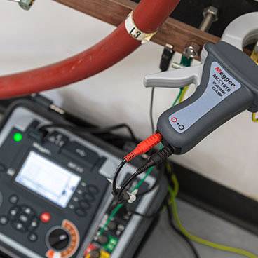 Multimeter and probes on a red cable, likely used for electrical measurement, with a blurred measuring device in the background.