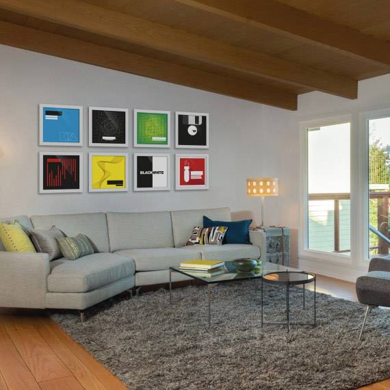 Living room with a grey sofa, beige carpet and modern artworks on the wall. A window with a view to the outside.