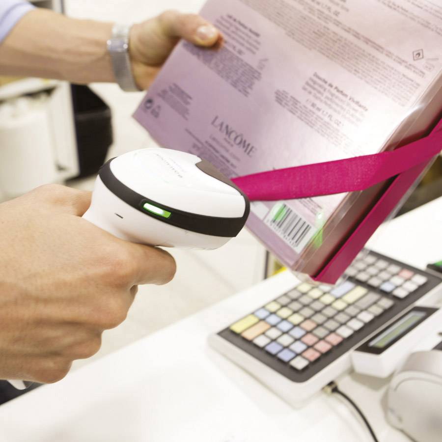 A person scans a product packaging with a barcode scanner at the till of a shop.