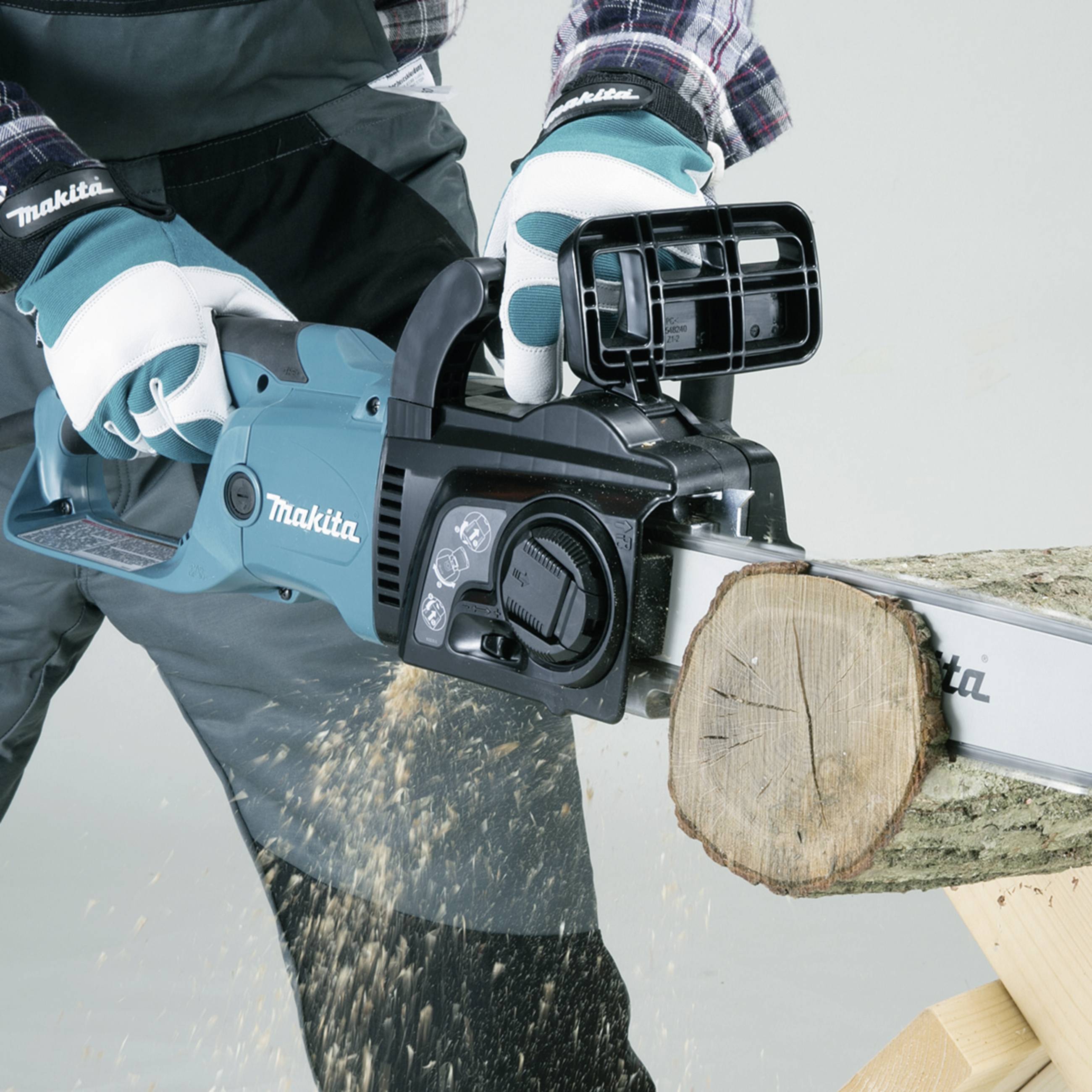 A person is sawing a wooden log with a blue Makita chainsaw. Sawdust is flying through the air.