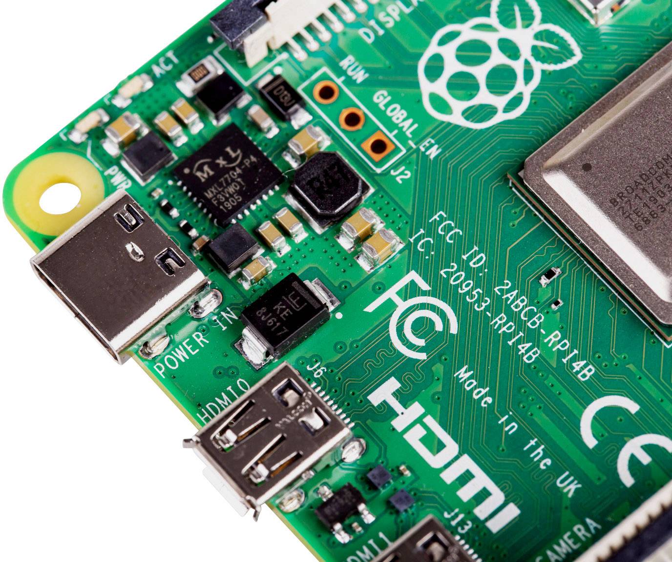 Close-up of a green circuit board with USB and HDMI ports. Raspberry logo in the top left corner. Text on the board: 'FCC ID: 2ABCB-RPI4B'.