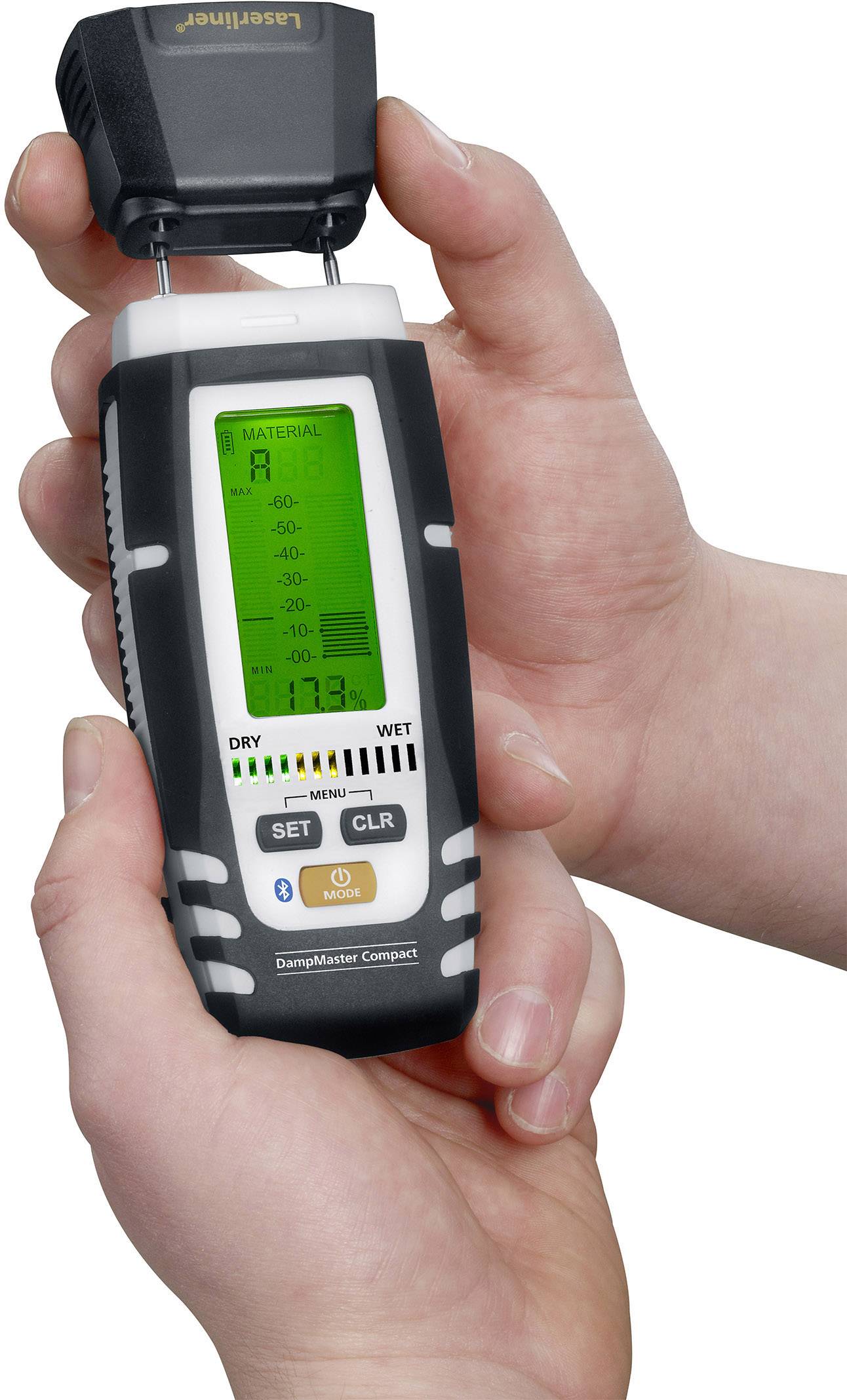 A person is holding a digital moisture metre with a green illuminated display. The device is showing moisture readings that fall between 'dry' and 'wet'.
