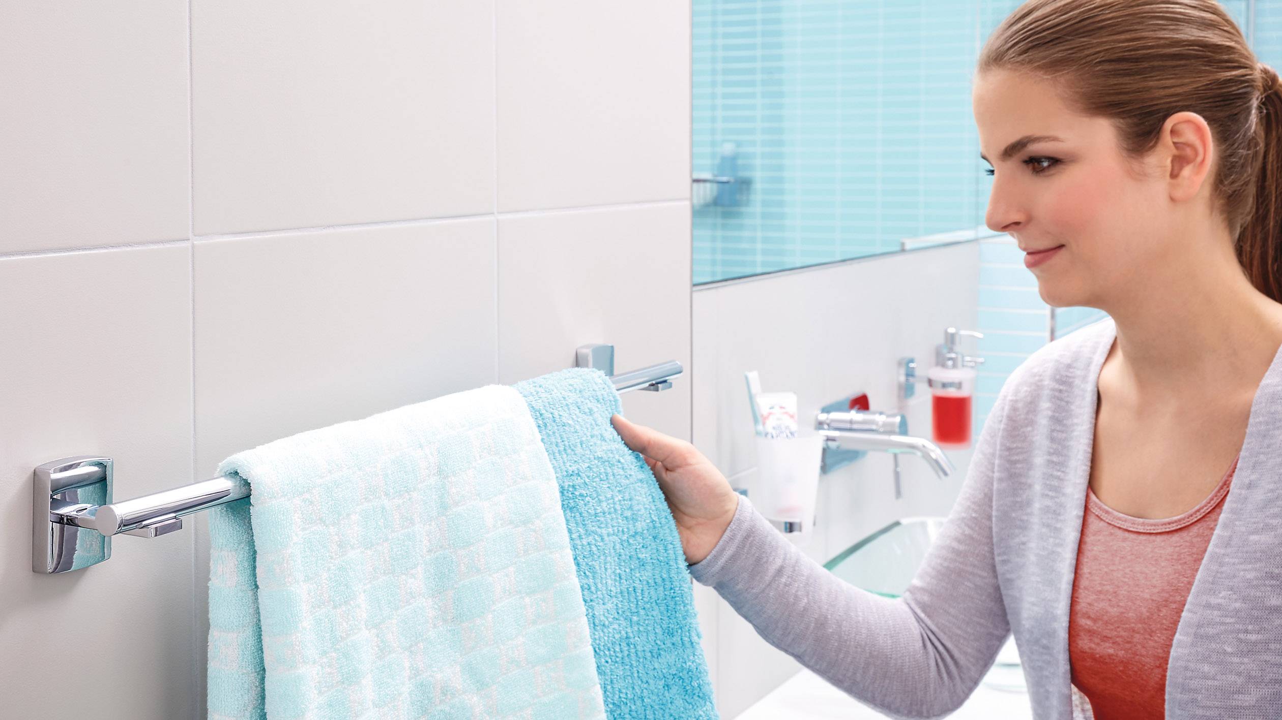A person is hanging a light blue towel on a towel rail in a modern bathroom with blue tiles.