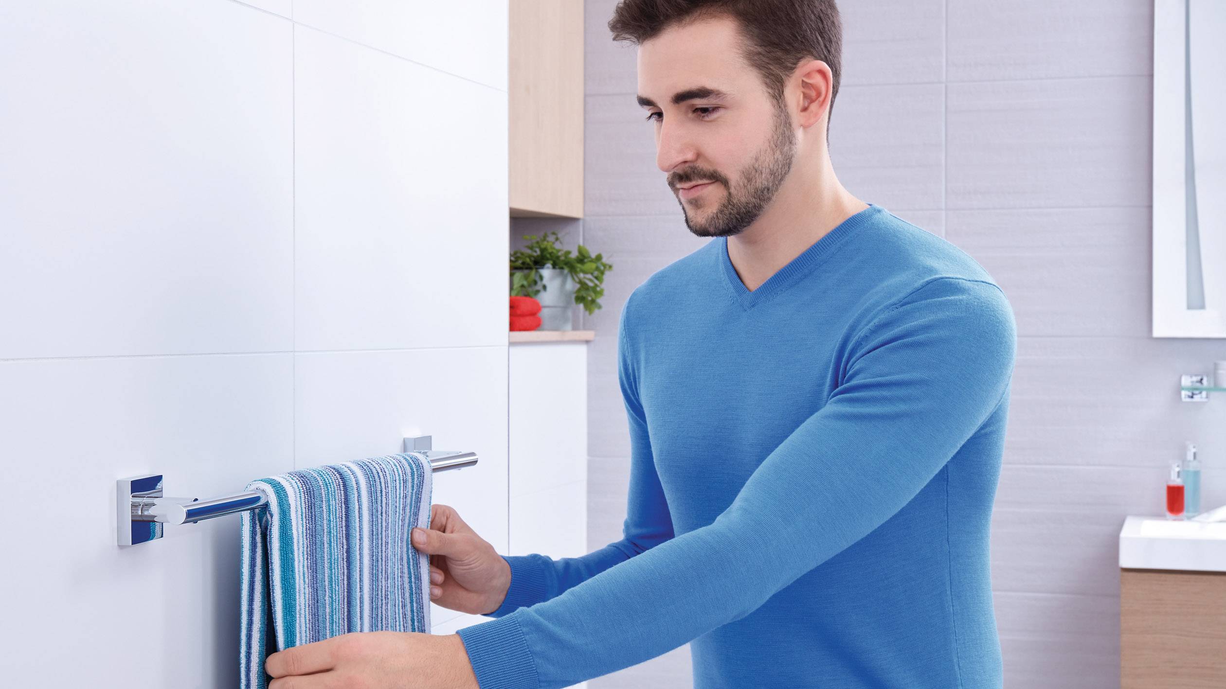 A man in a blue jumper is hanging a striped towel in a modern-designed bathroom.