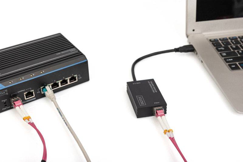 A laptop is connected to a network device via an ethernet cable. Both devices are shown against a white background.