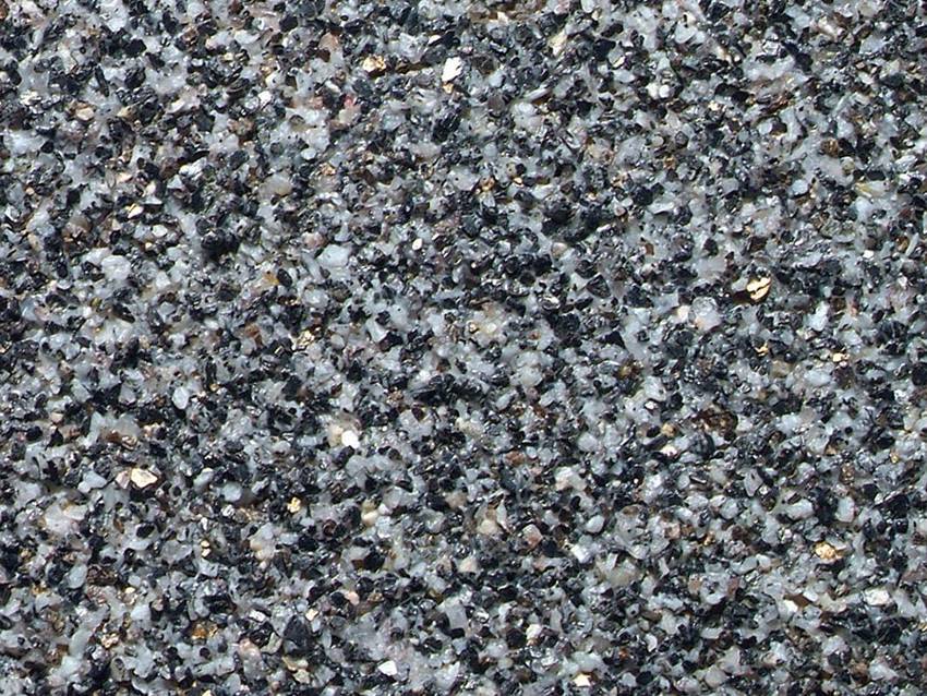 Close-up of an asphalt surface with a coarse-grained texture, composed of small, multicoloured stones and gravel.
