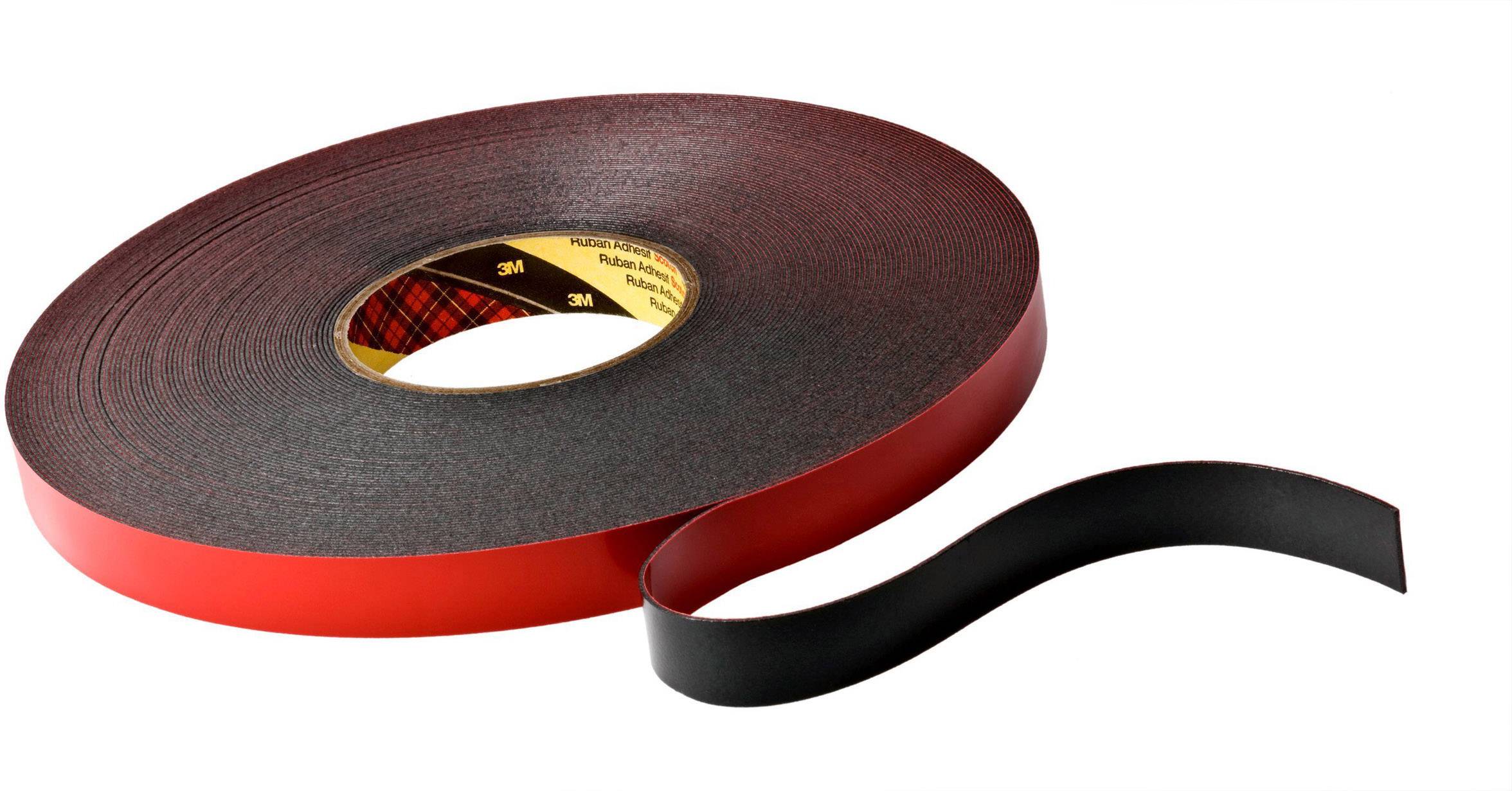 A large roll of black double-sided adhesive tape with a red protective strip, partially unrolled.