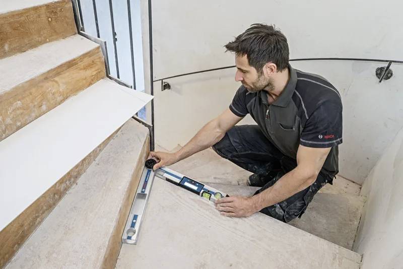 A person measures a staircase using a digital level, possibly for renovations, highlighting precision in construction work.