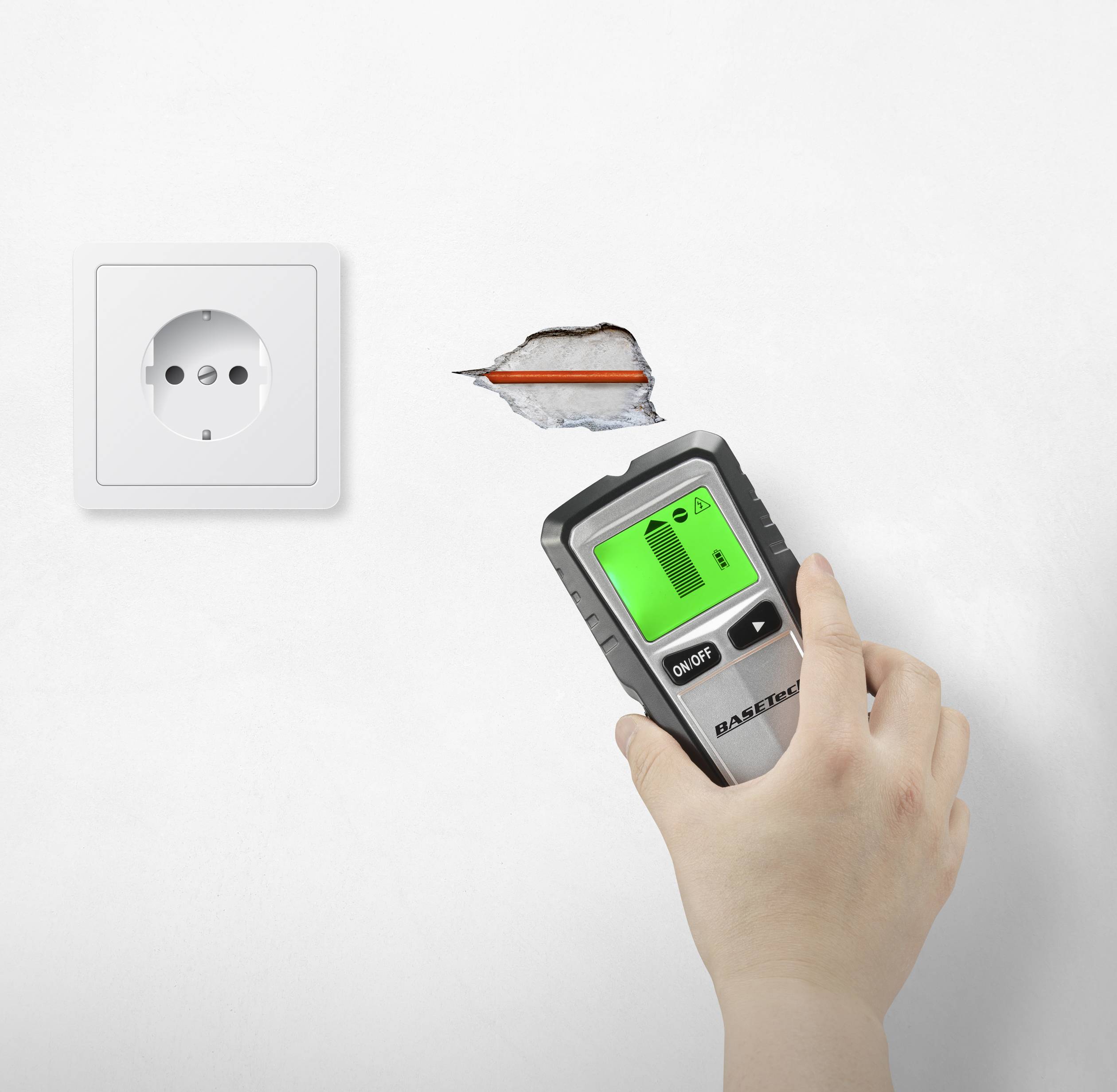 A hand is holding a cable detector over a hole in the wall next to a power socket. The cable detector is displaying a warning on its screen.