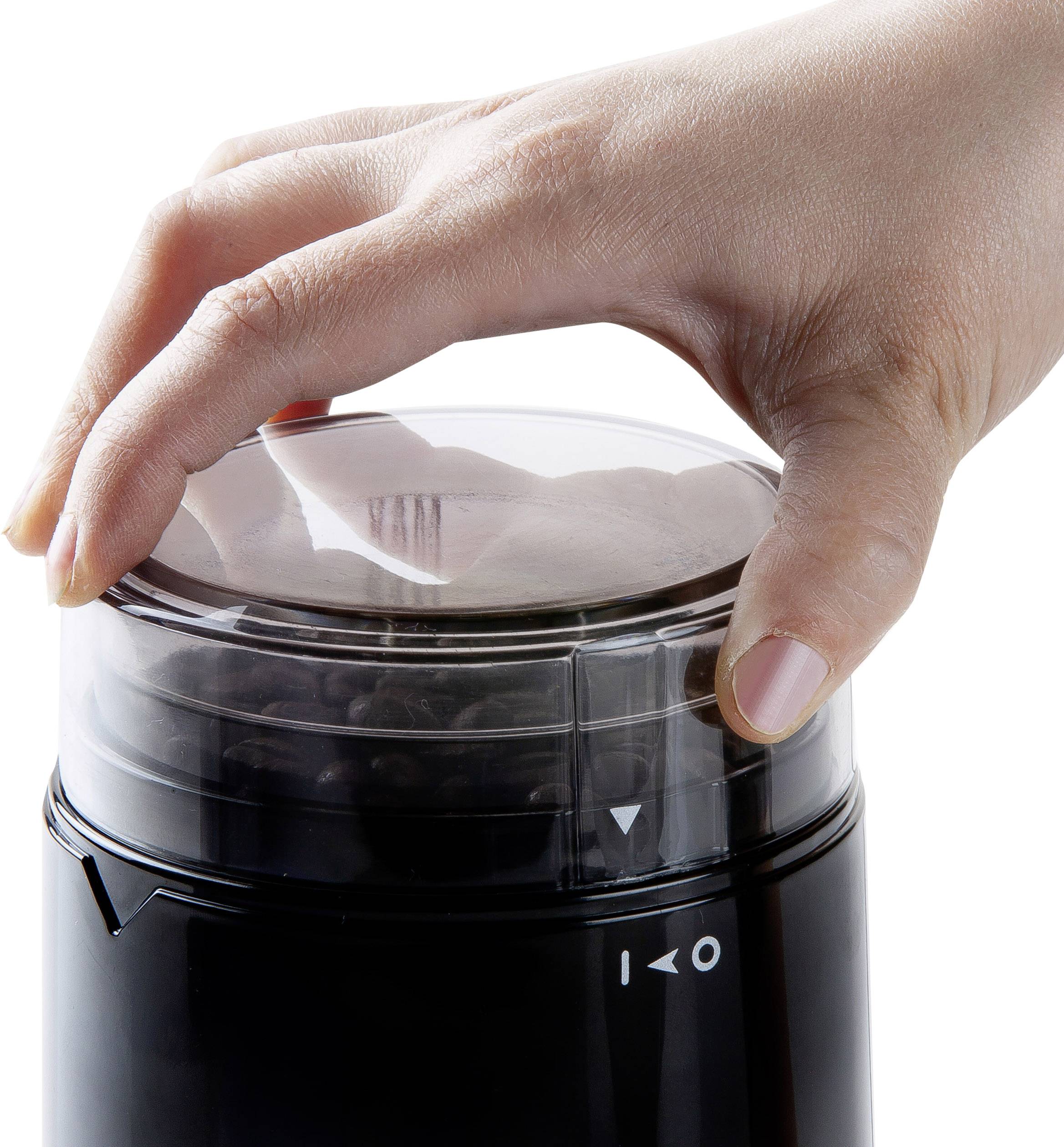 A hand presses down on the lid of a black electric coffee grinder with ground coffee visibly contained within.