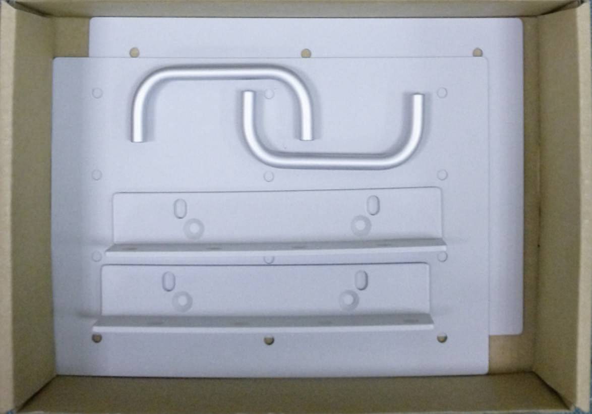 A cardboard box containing white, rectangular metal plates with holes and curved handle bars, presumably intended for assembly.