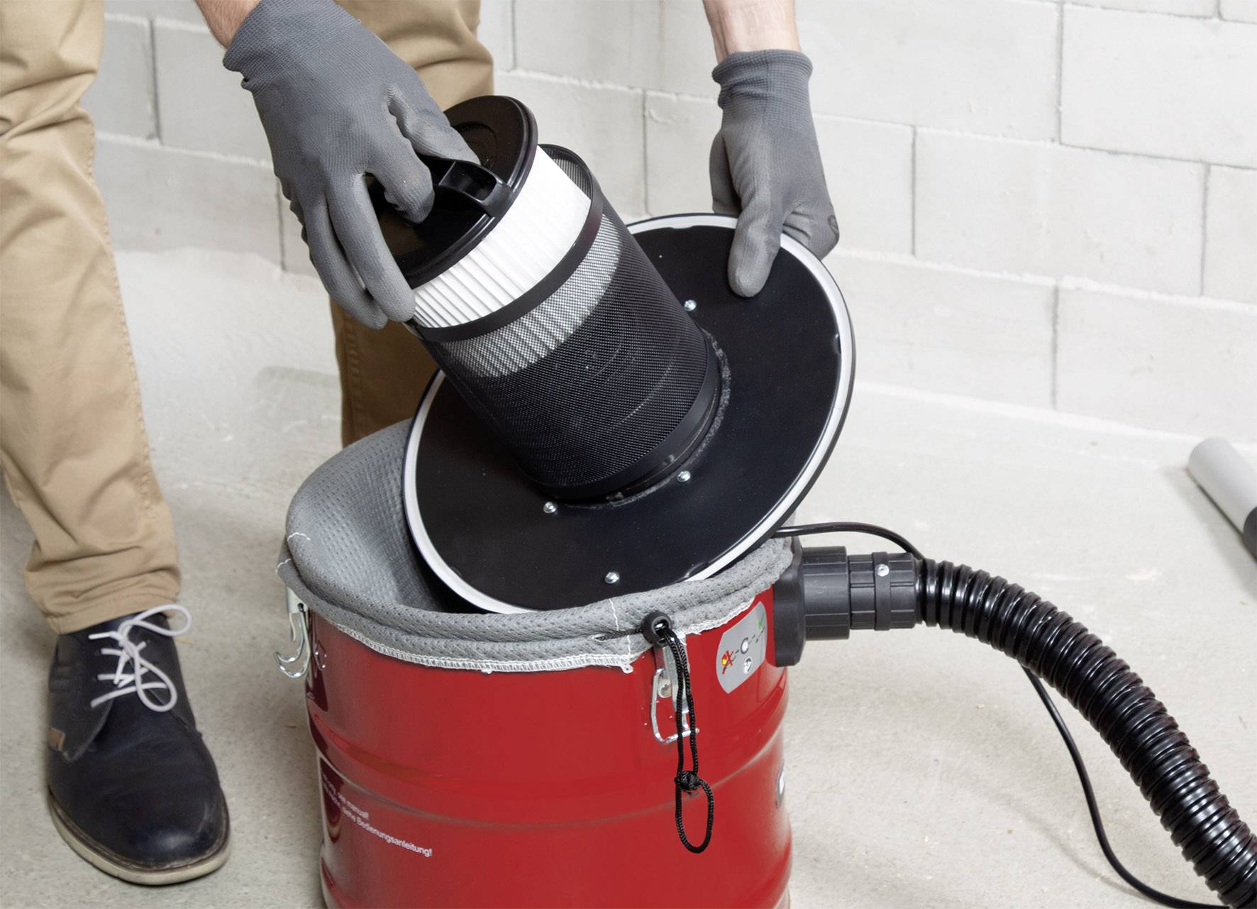 A person is changing the filter of a red vacuum cleaner in a workshop environment.