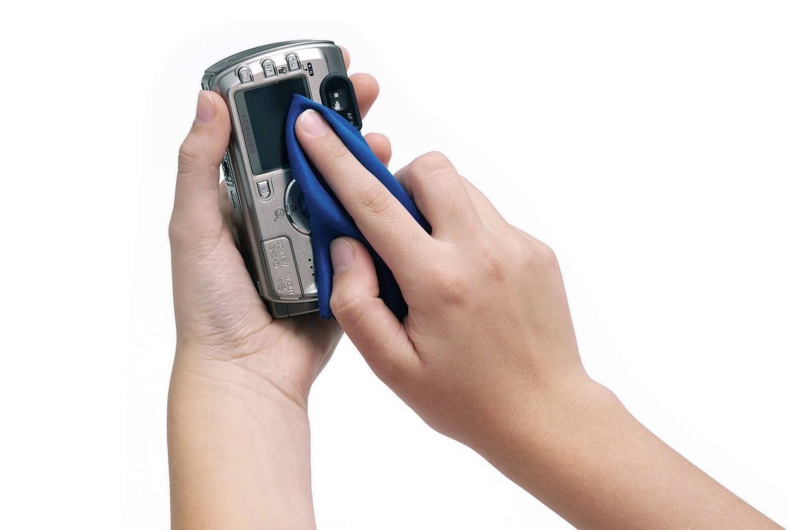 Two hands holding a digital camera; one hand cleans the lens with a blue cloth.
