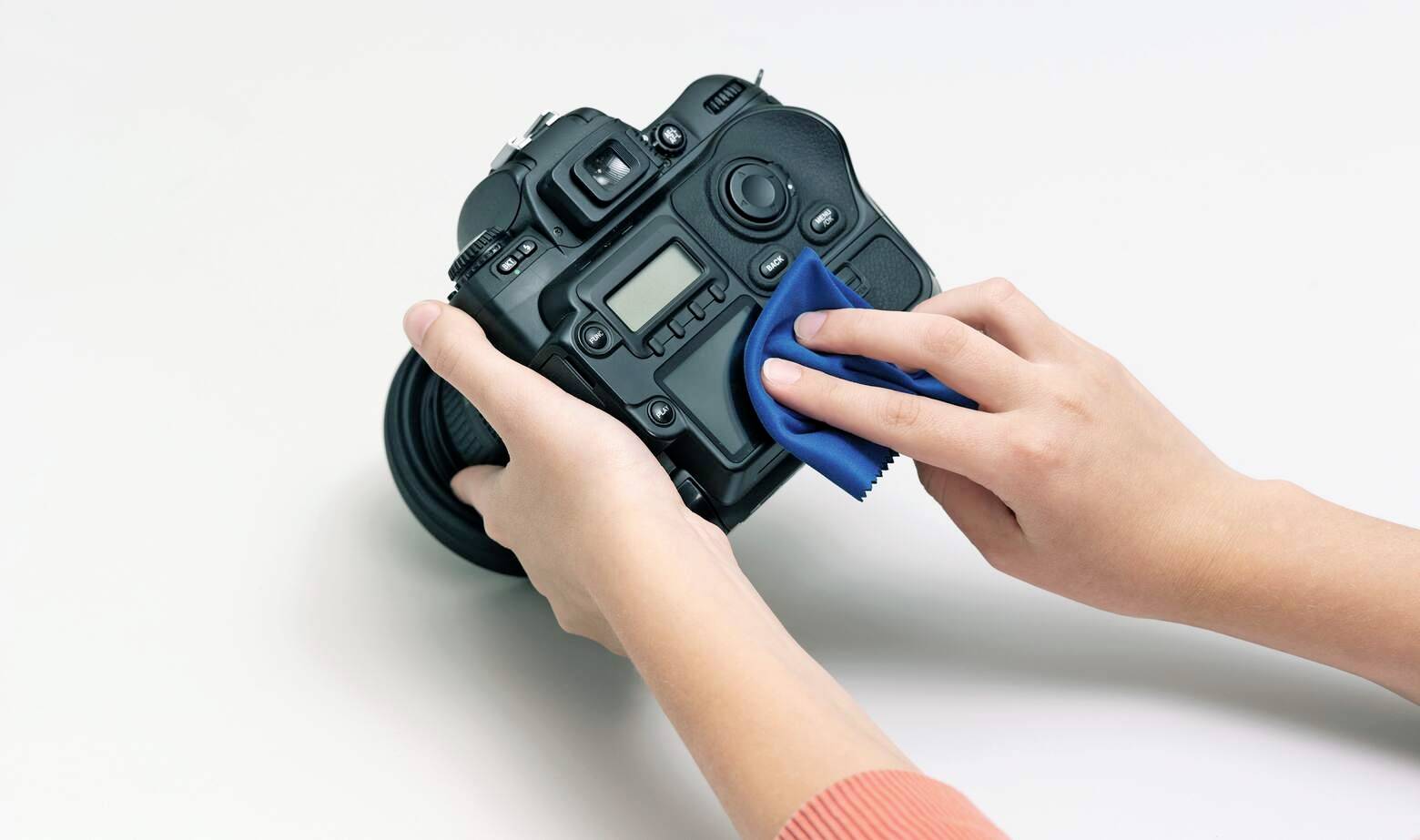 Hands cleaning a camera with a blue cloth, illustrating proper maintenance.