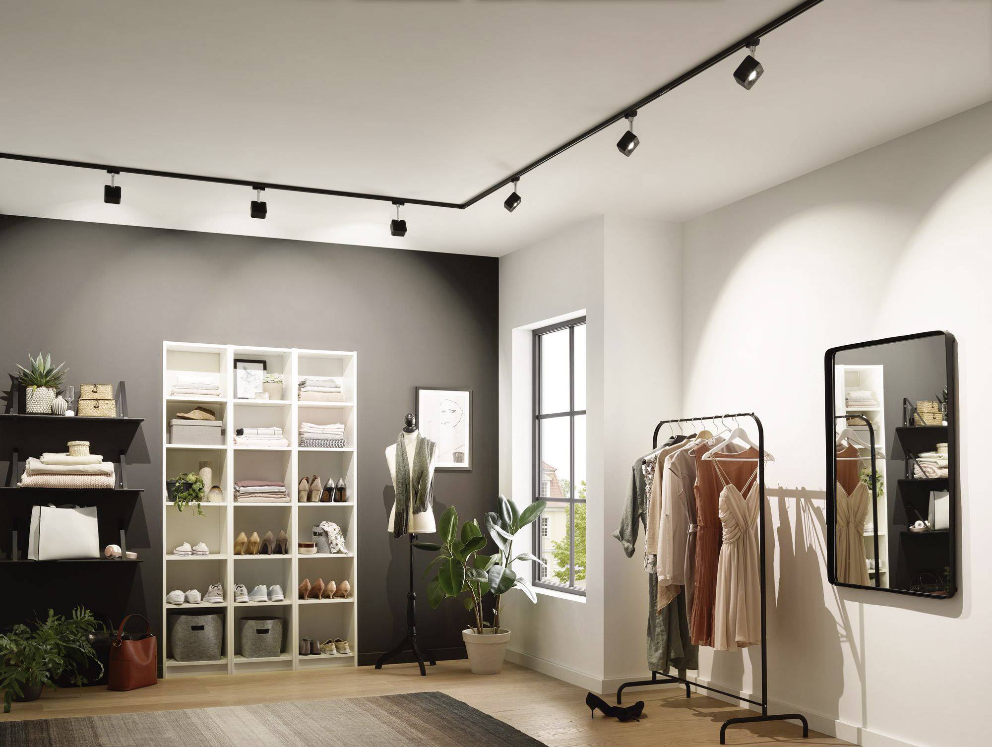 A modern clothing shop with shelves full of garments and shoes, a mannequin and a mirror beside a window.