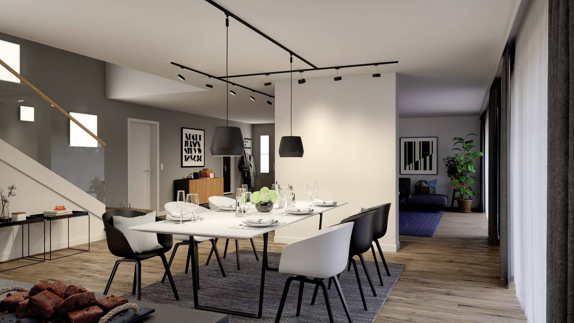 A modern furnished dining room with a long table, six chairs and stylish lighting. In the background, a staircase and decorations are visible.