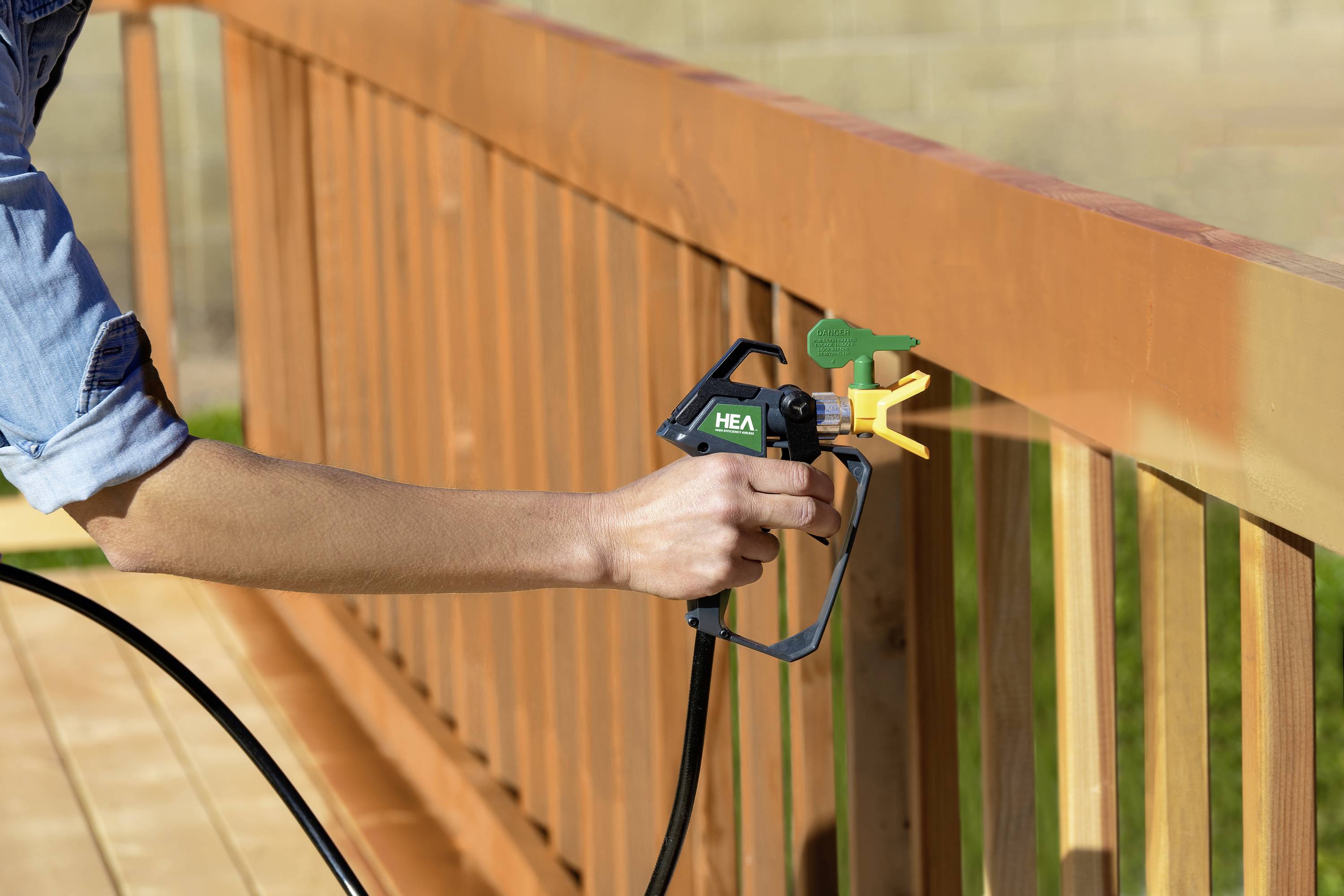 A person is painting a wooden banister with a spray gun. The banister is already partially painted and has a reddish-brown colour.