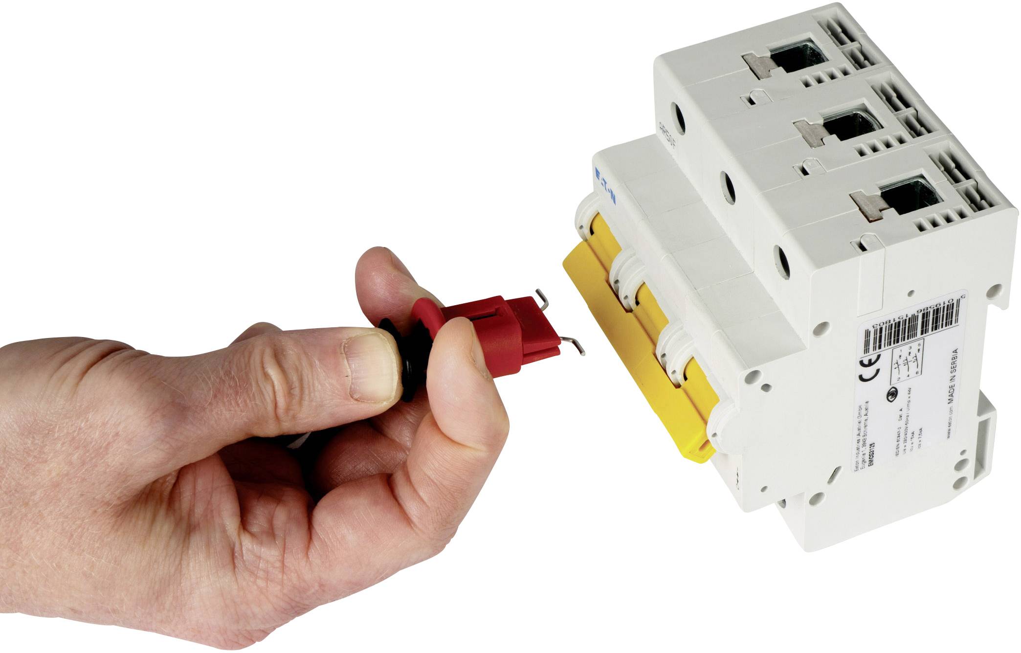 A hand is holding a red testing adapter towards a white electrical protection switch with three switches.