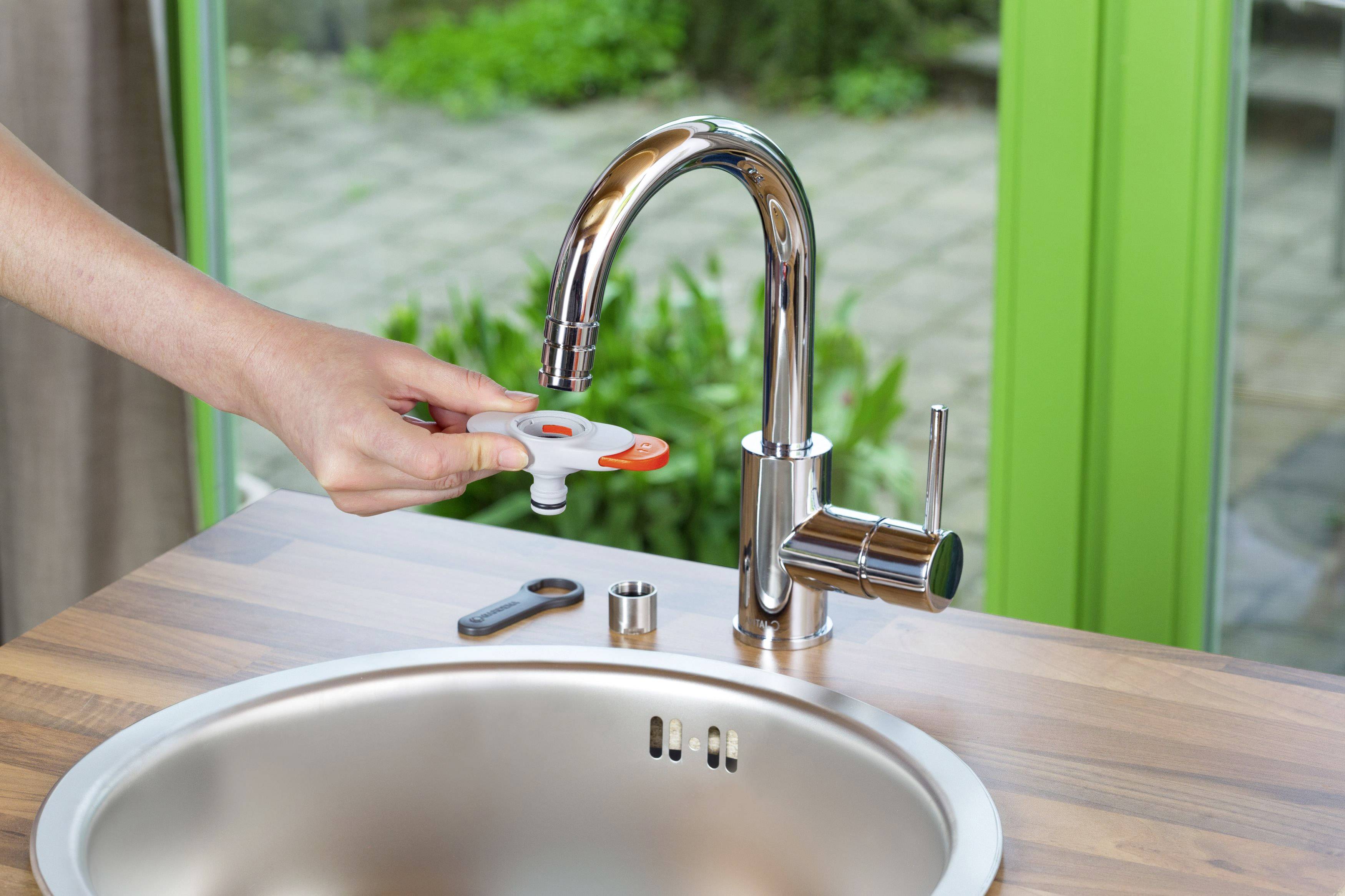 A person is replacing the aerator of a tap in a modern kitchen to conserve water.