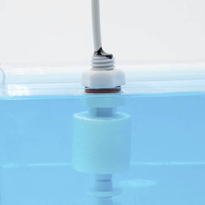 A white cylindrical float valve in a tank of blue liquid, part of a water level control system.