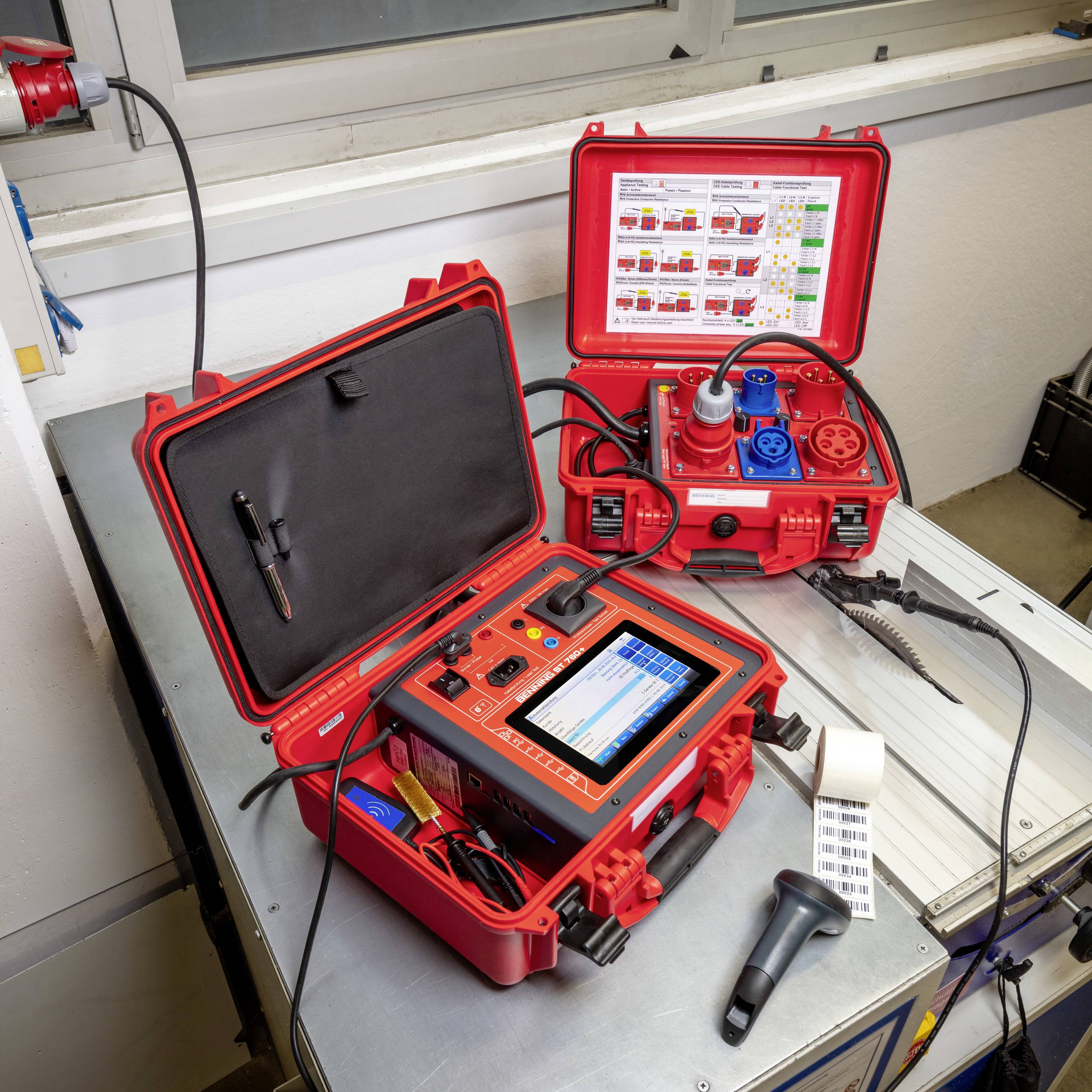An open testing device with cables and a digital display on a table, with another closed device and labels nearby.