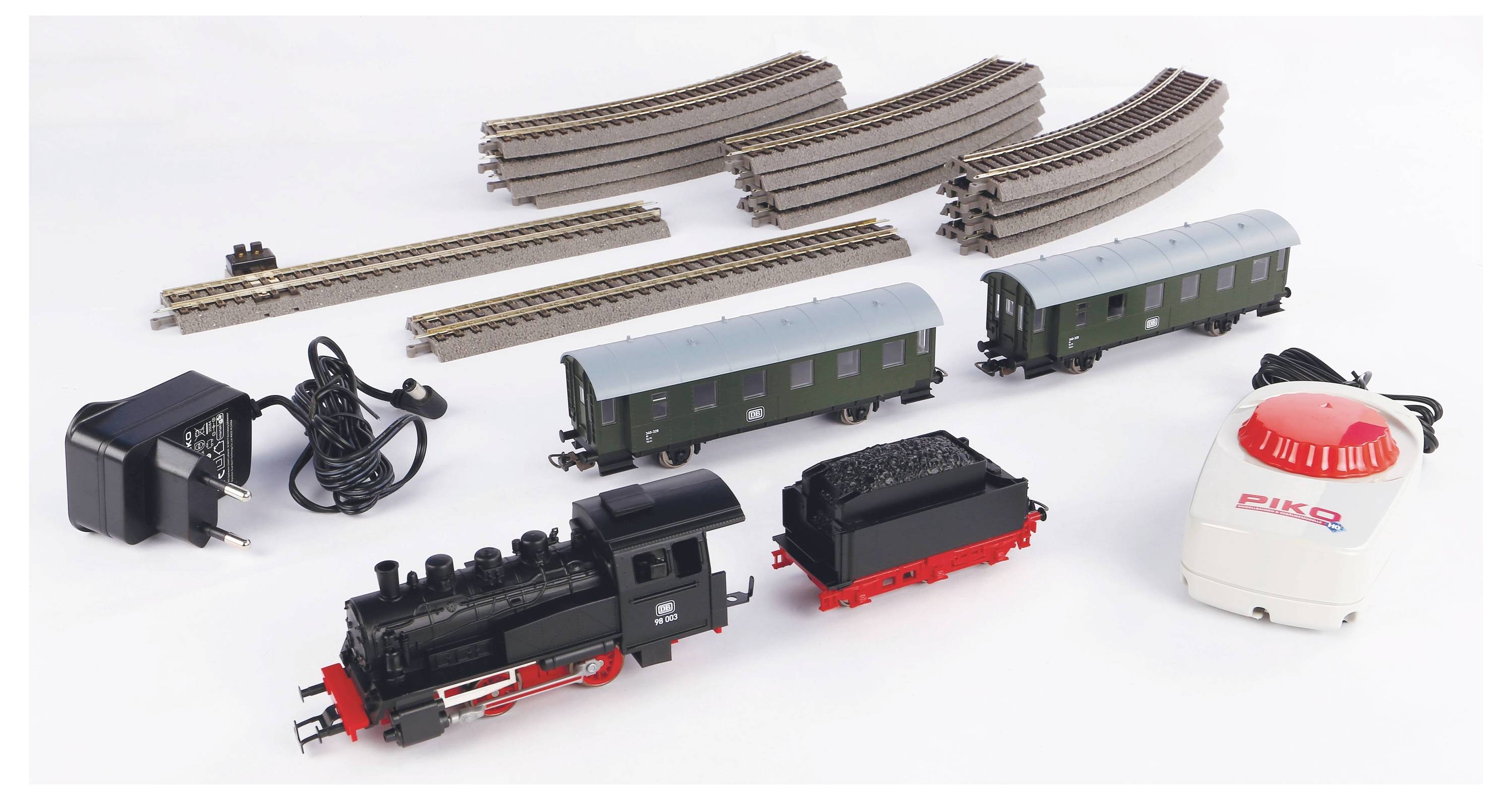 Model railway set with tracks, two carriages, locomotive, control unit, and power supply. Tracks in curved and straight configurations.