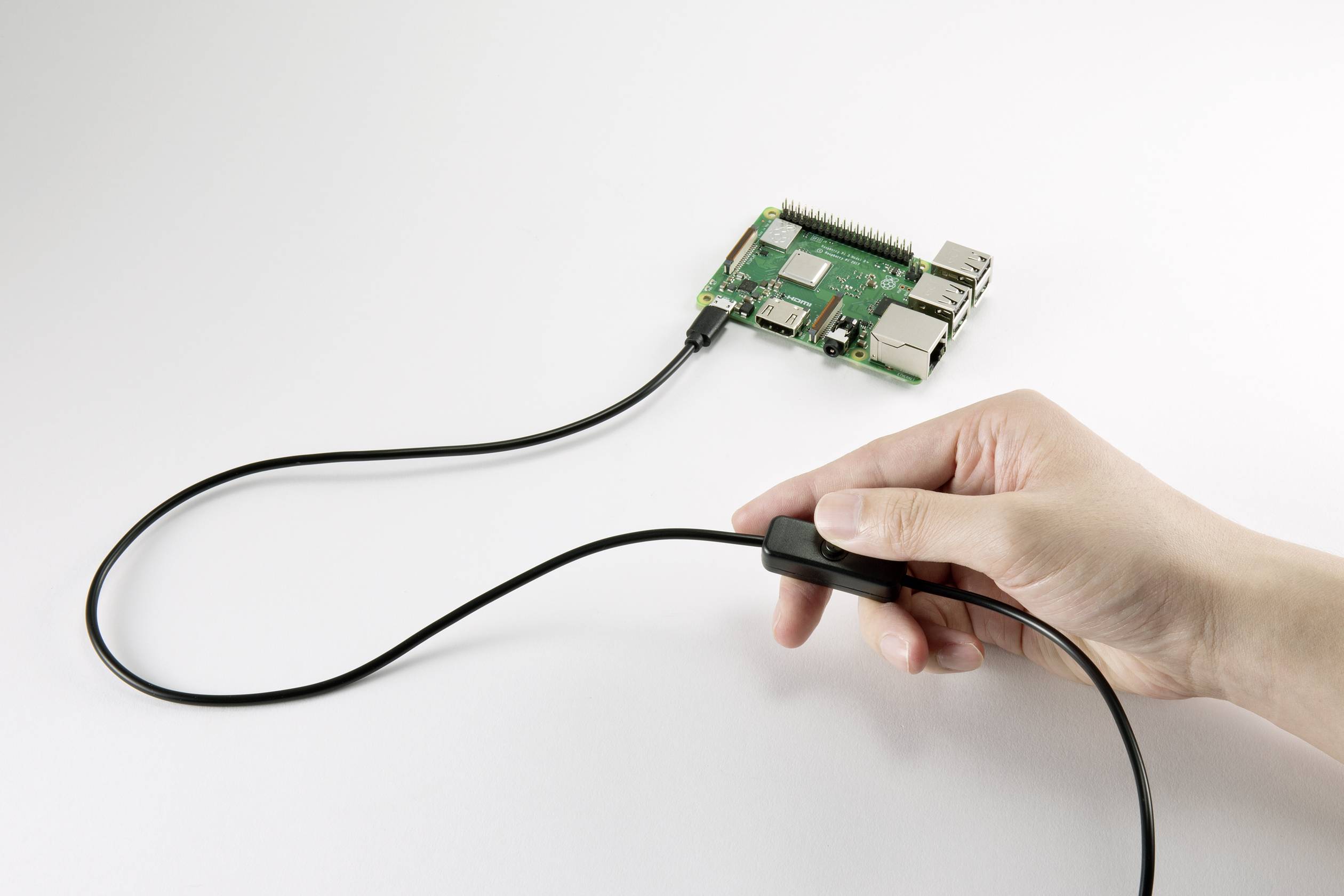 A hand is holding the plug of a cable connected to a microcomputer. The microcomputer is resting on a white surface.