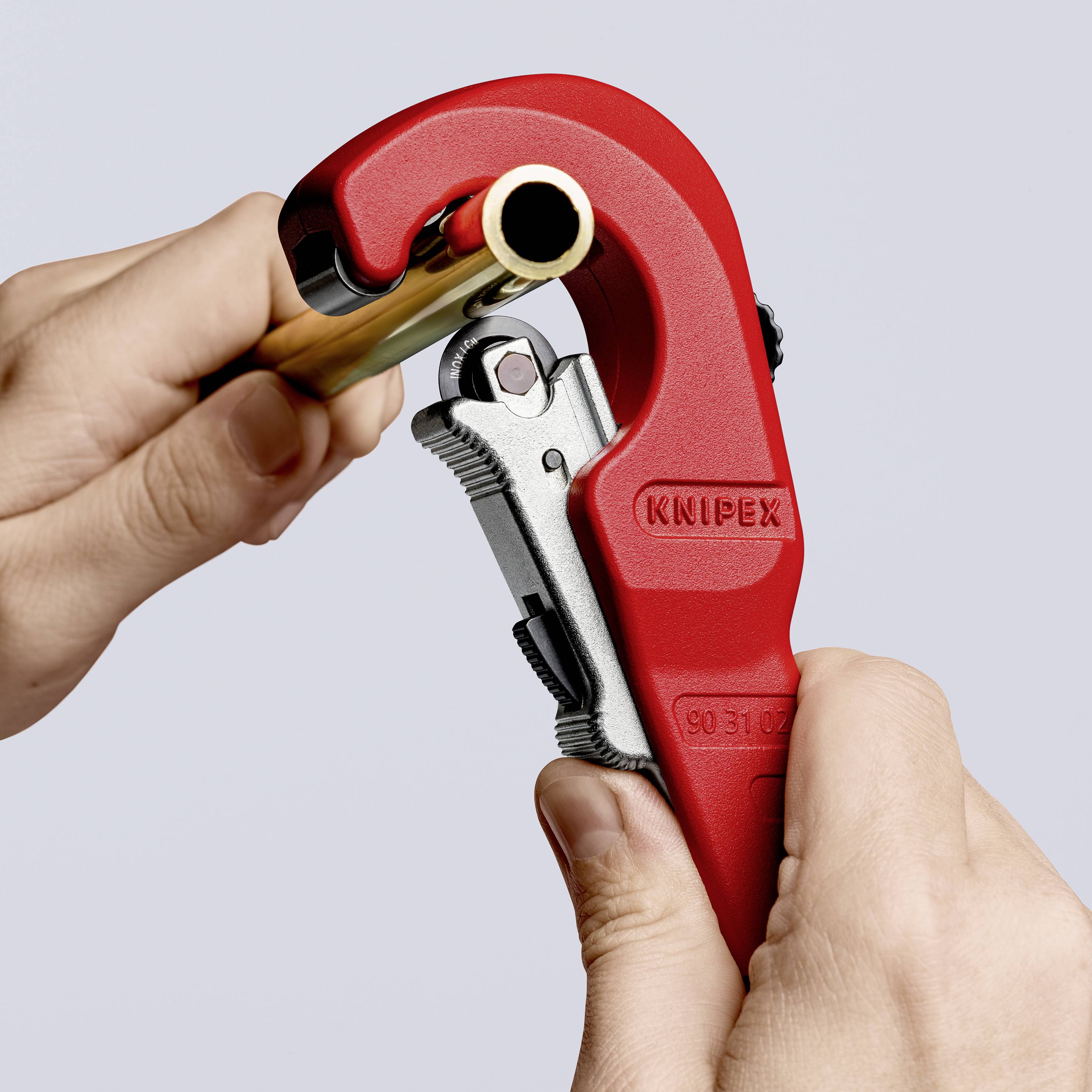 A hand is using a red pipe cutting tool to cut a pipe. The brand name 