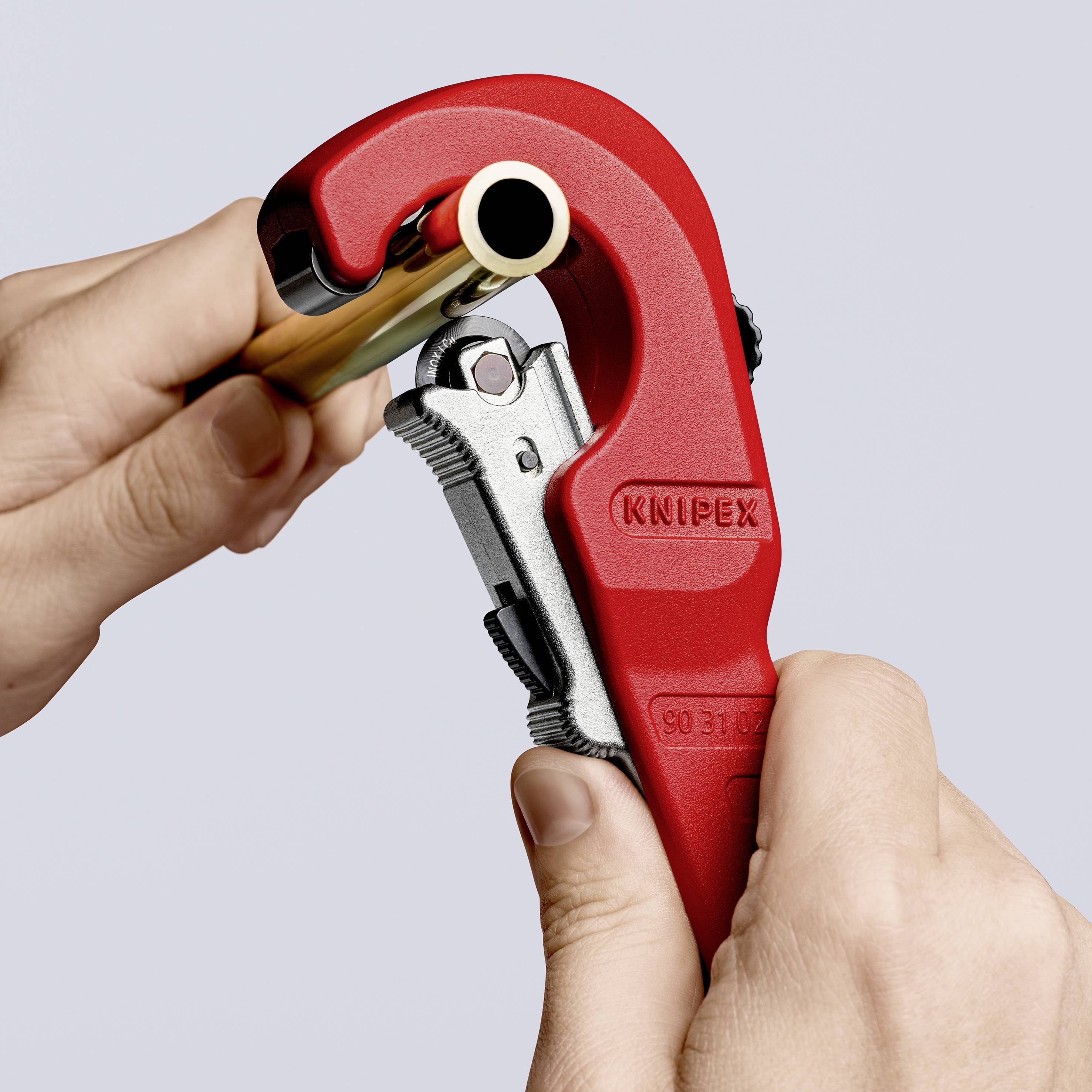 A person is cutting a pipe with a red pipe cutter tool. The tool bears the inscription 'Knipex'.