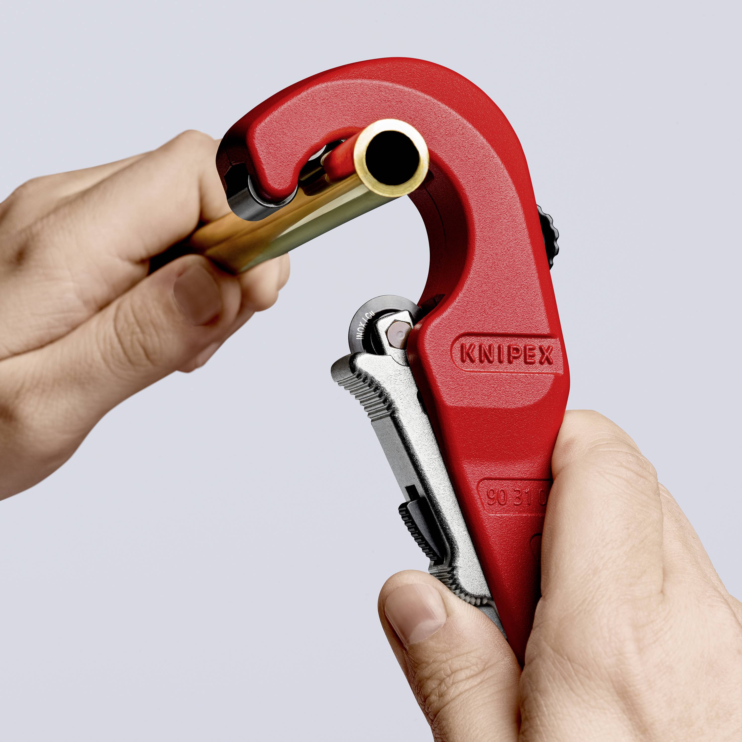 A hand holds a KNIPEX pipe cutter while cutting a pipe. Close-up of the tool in use.