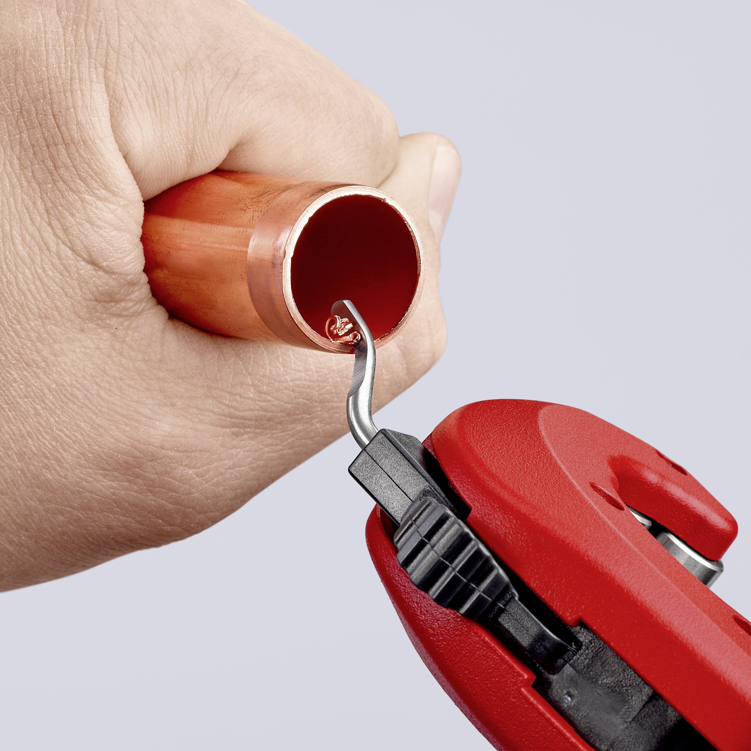 Hand holding copper pipe; deburring tool being used to smooth the inner edge.