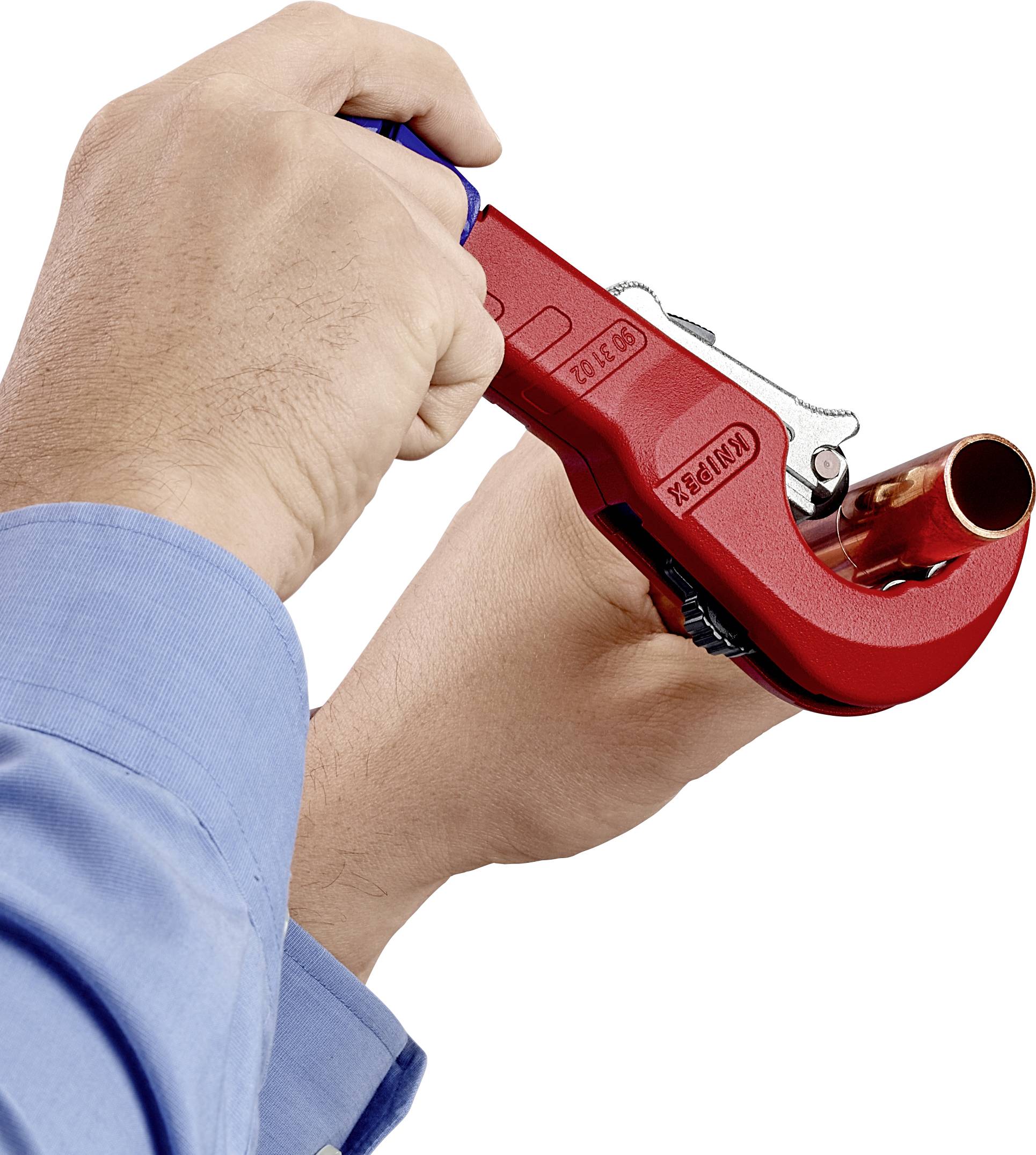 A hand is holding a red pipe cutter which is cutting through a copper pipe. The cutting process is in progress.