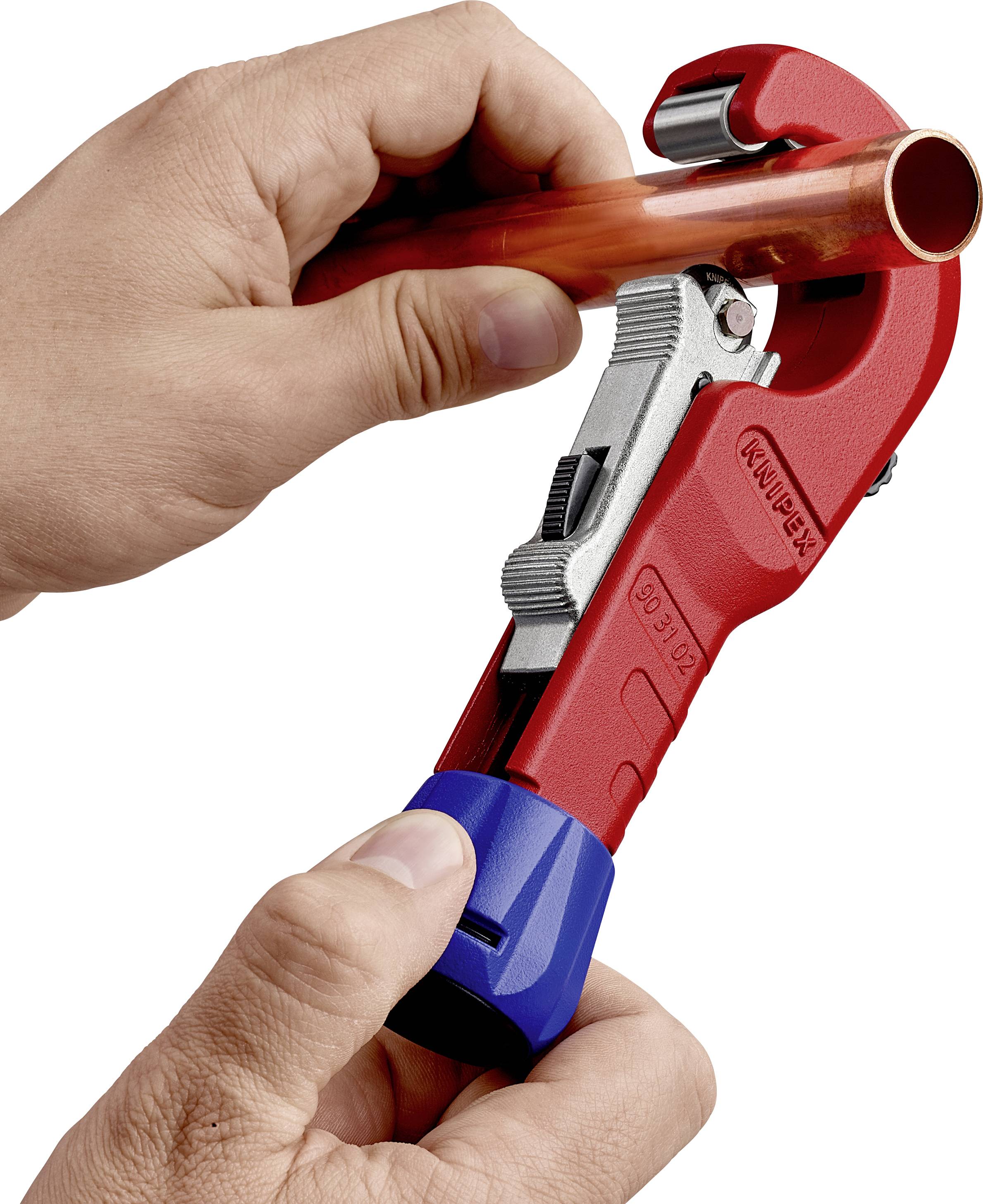 A hand is holding a pipe cutter tool and cutting a copper pipe. The tool is red with a blue handle.
