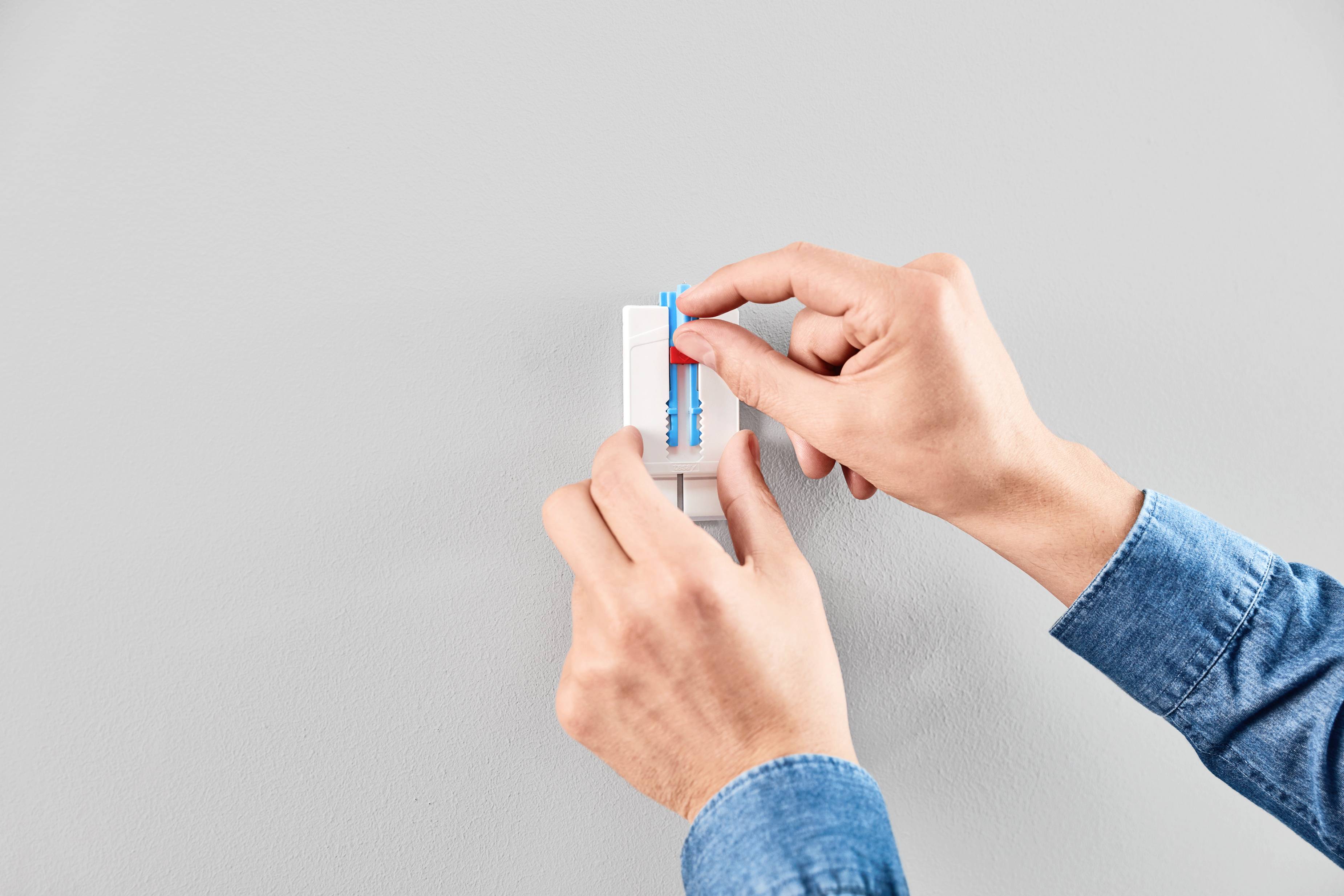 Hands of a person operating a light switch on a grey wall. The individual is wearing a blue shirt.