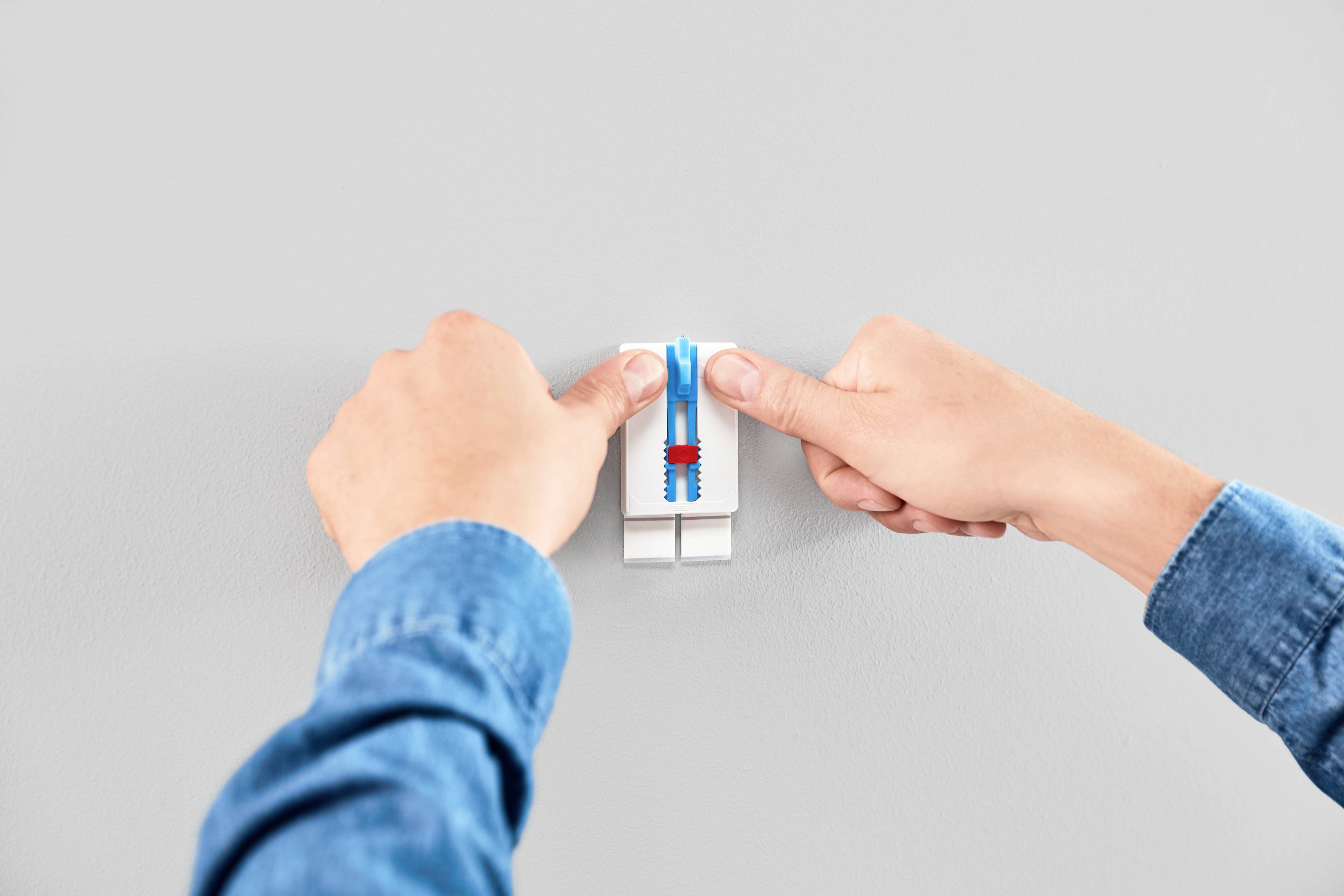 Two hands are pressing a light switch on a smooth, light grey wall.