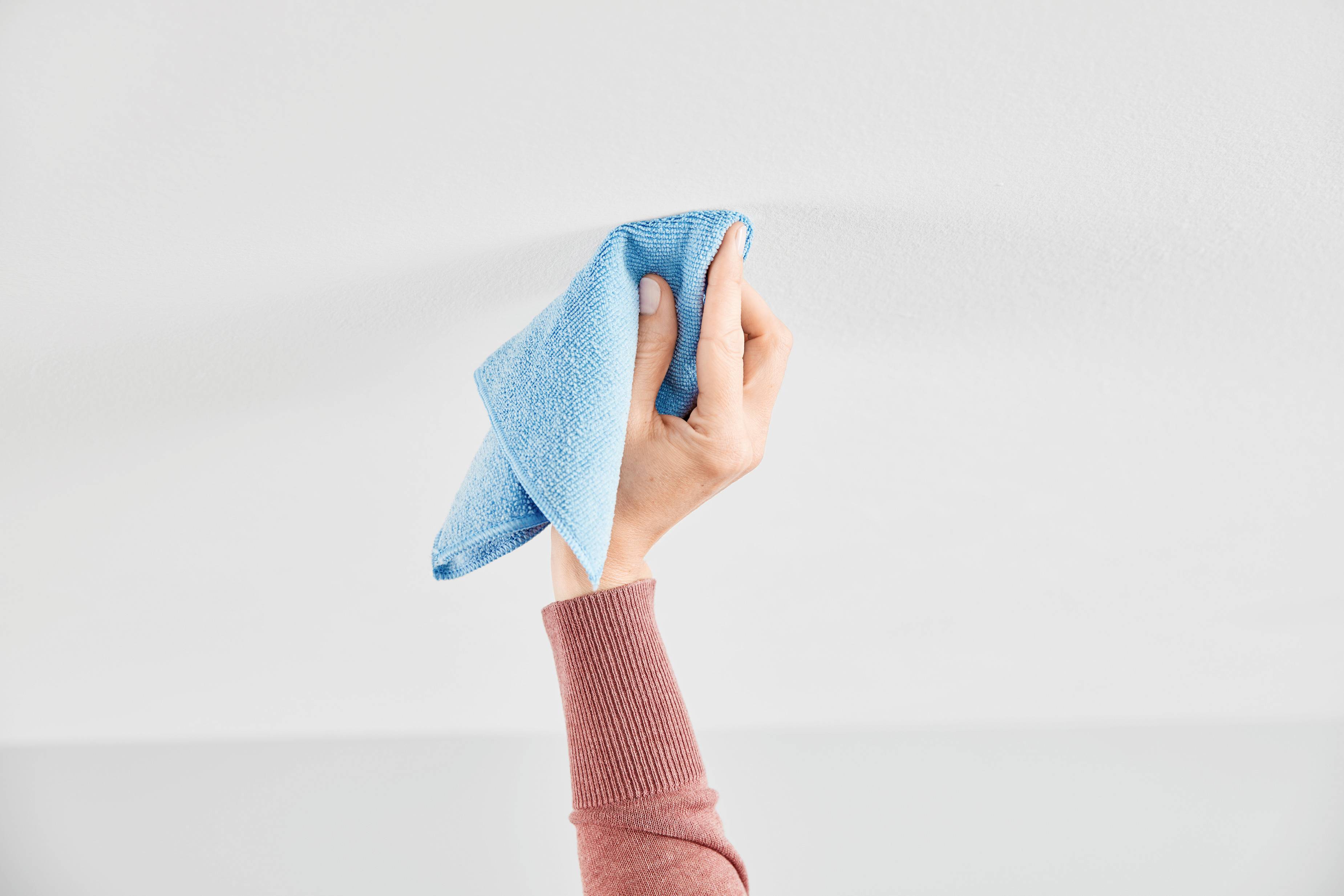A hand in a red jumper holds a blue cloth and wipes a white surface.