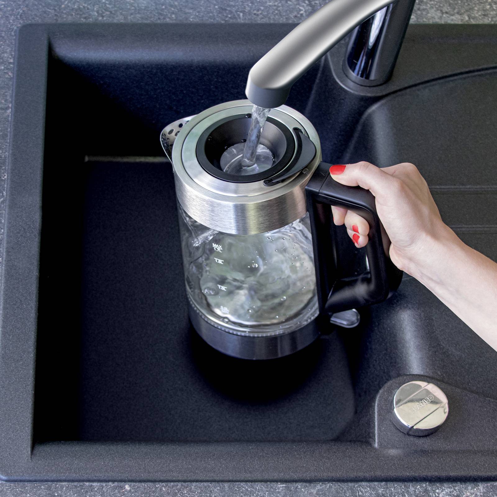 A person is holding a kettle under a tap in a sink while water is flowing into the kettle.