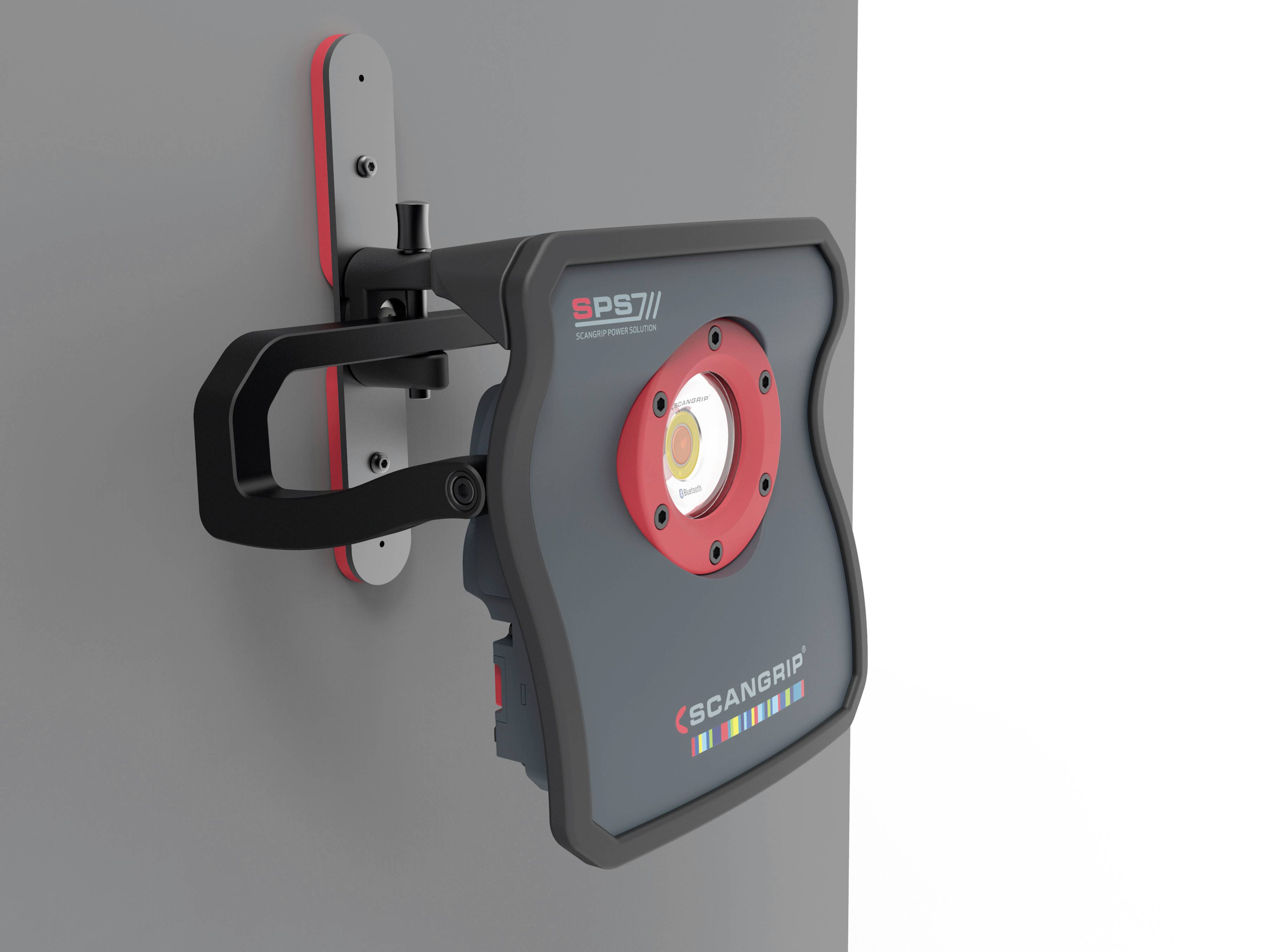 A black and red LED lamp is mounted on a grey holder on a wall. The device bears the inscription 'SCANGRIP'.