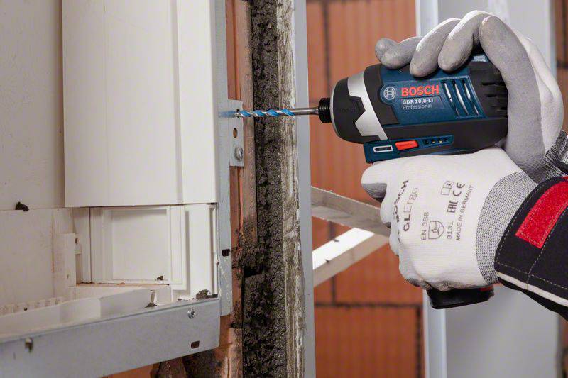 A person is drilling into a wall with a Bosch cordless drill. They are wearing protective gloves and positioning the drill straight.