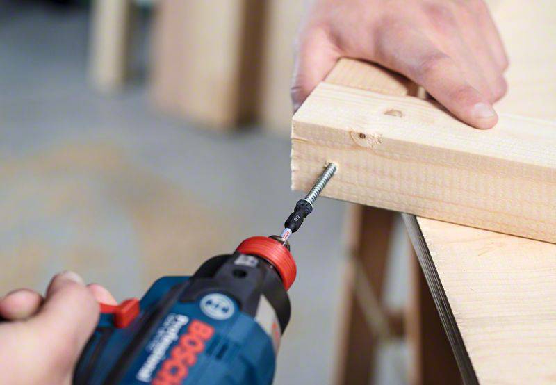 A person is securing two pieces of wood with a screw and an electric screwdriver. Hands are holding the wood steady.