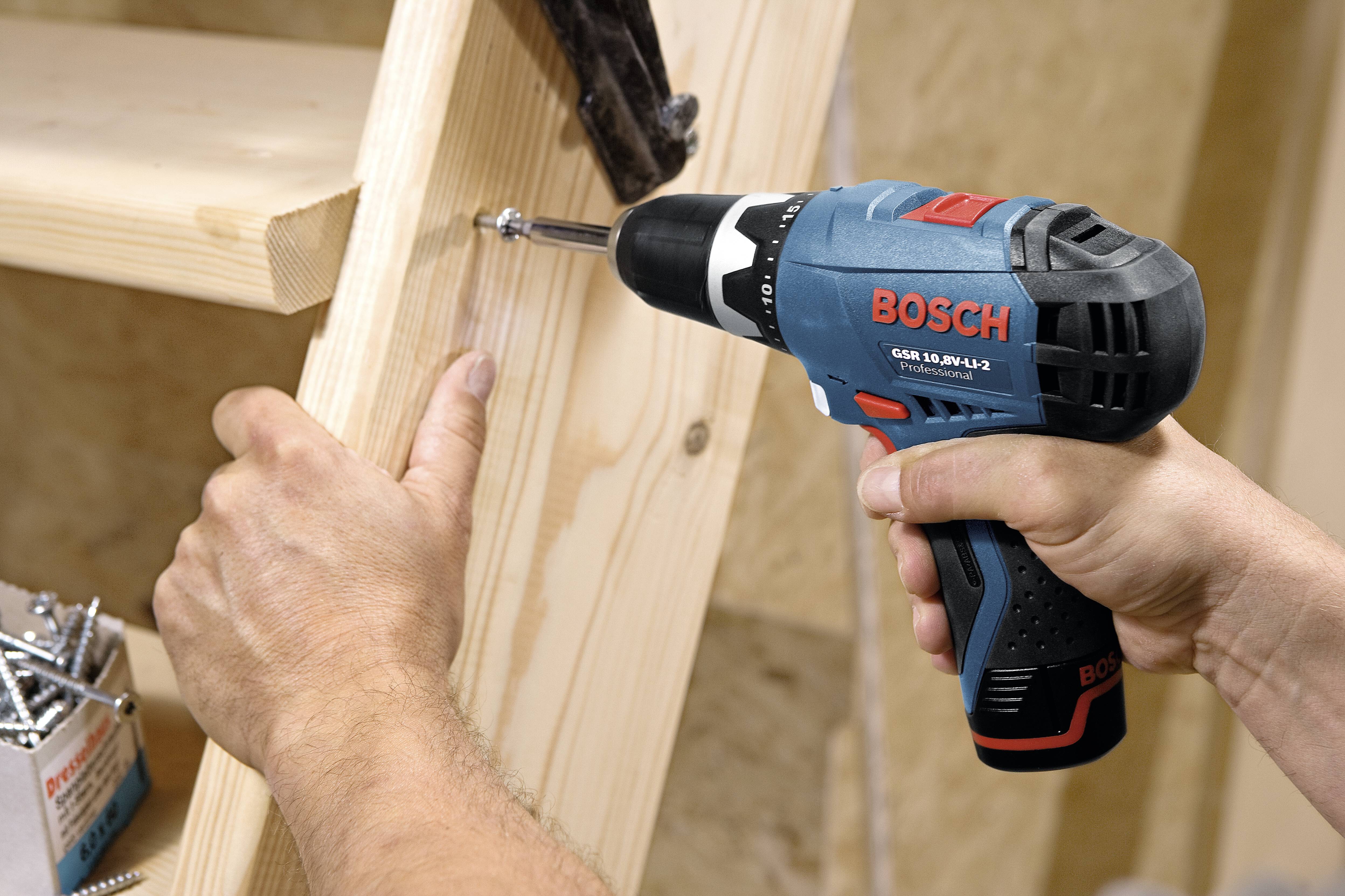 A person is using a blue power drill to screw a screw into a wooden board.