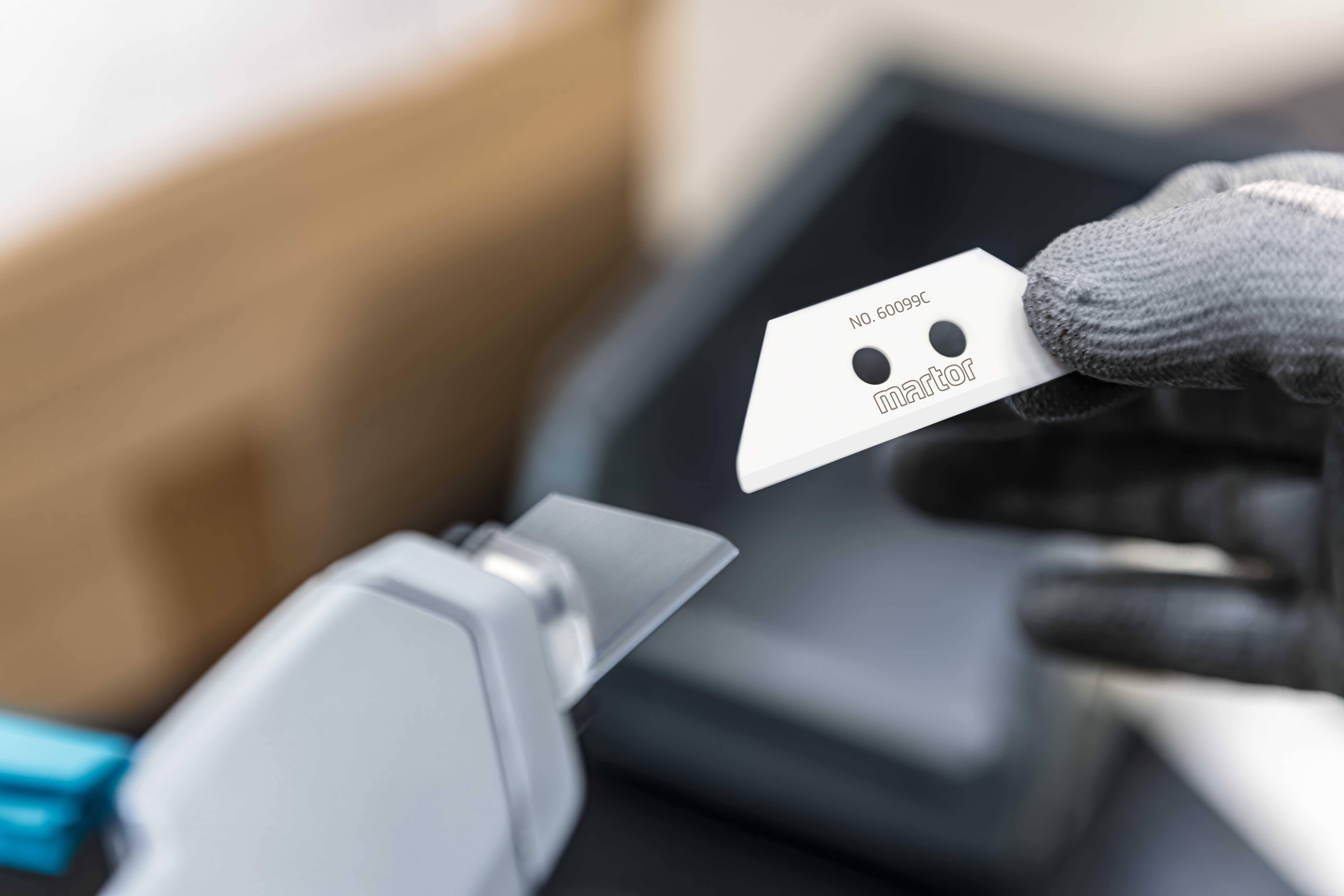 A person wearing gloves is holding a sharp blade, presumably for a cutting tool, in their hand.