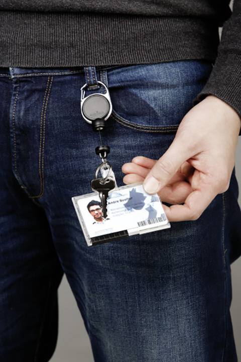 A person is holding a photo ID, attached to a clip, in front of their jeans. The ID contains a barcode and text.