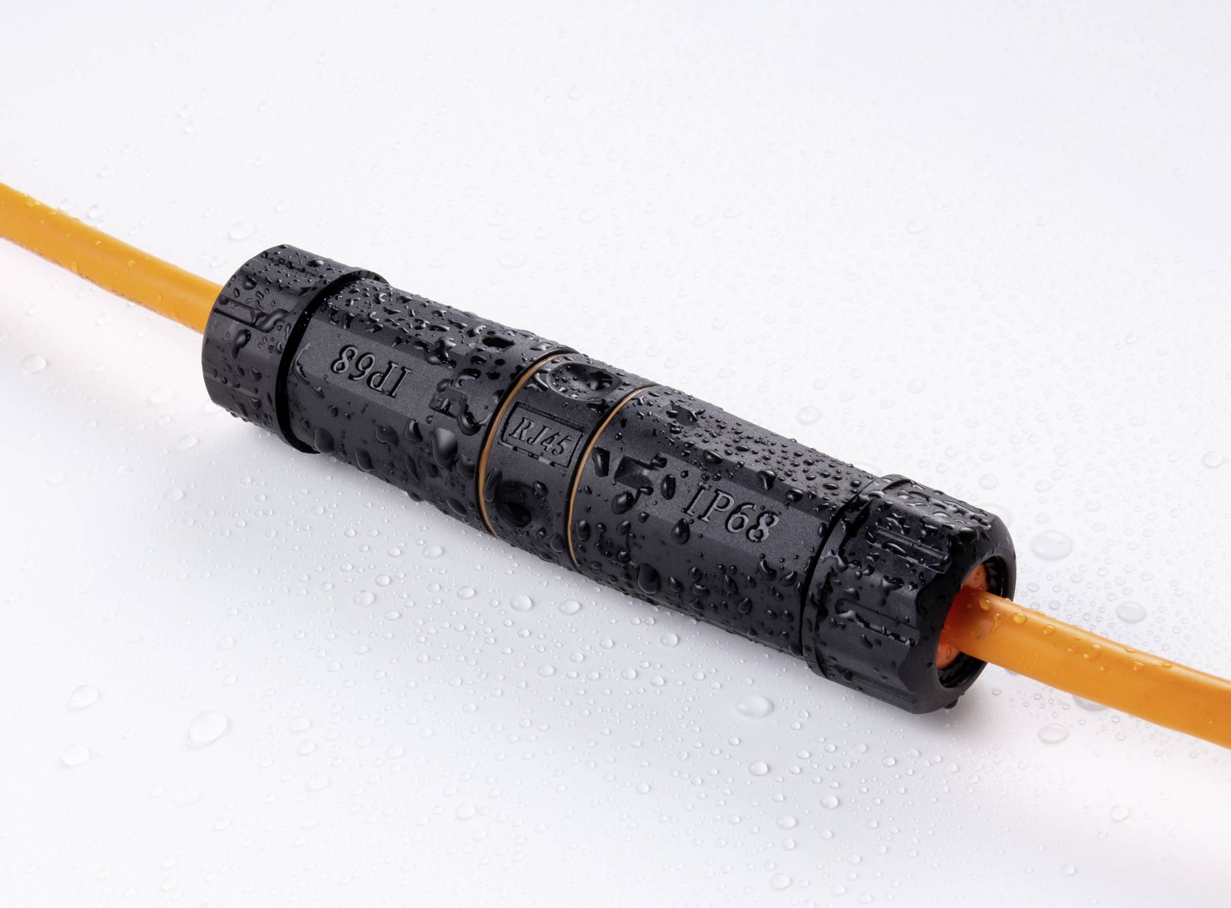 A black, waterproof cable connector with an IP68 label connects orange cables, surrounded by water droplets on a white background.