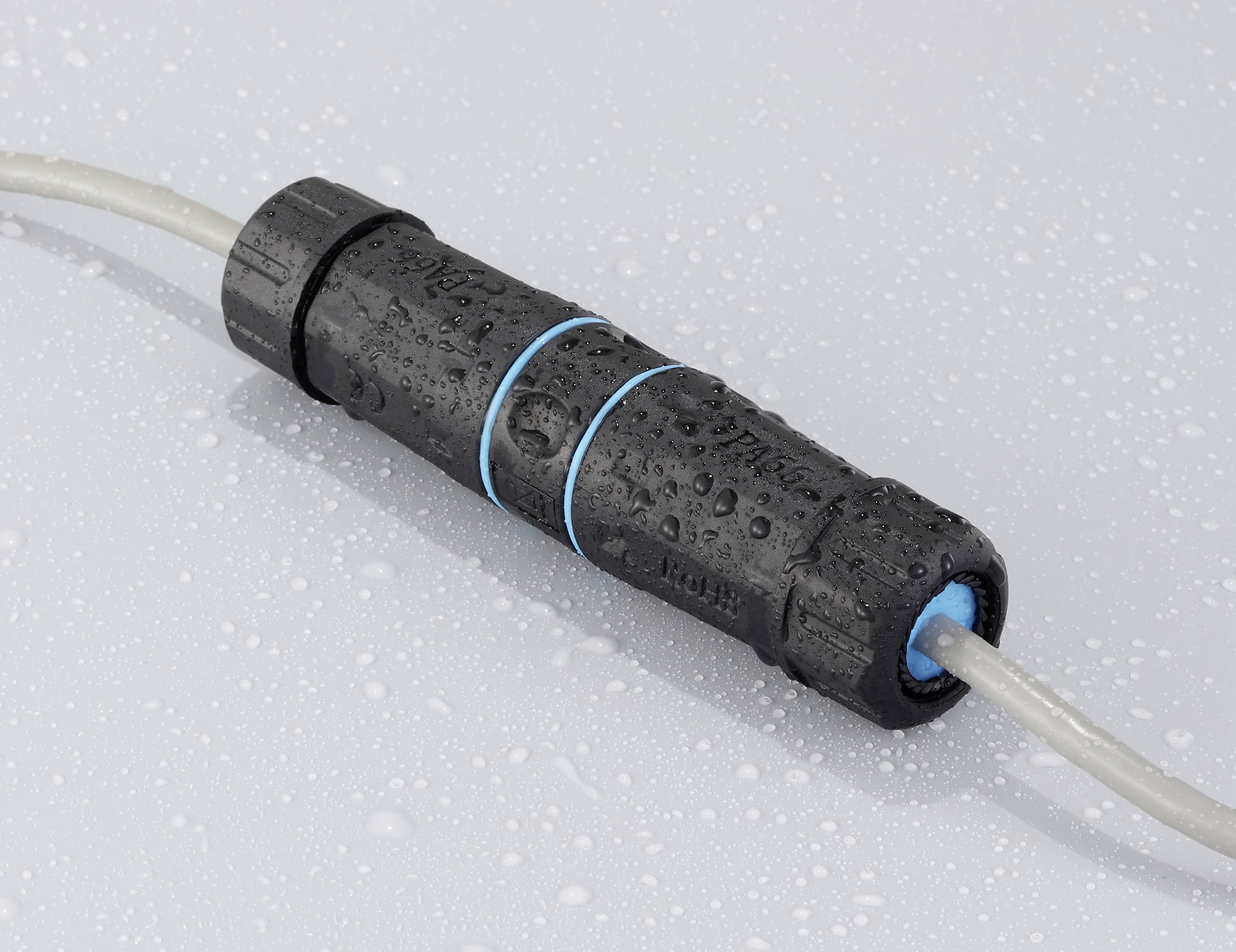 A black, waterproof coupling sleeve with blue rings, wet with water droplets, connects two grey cables.