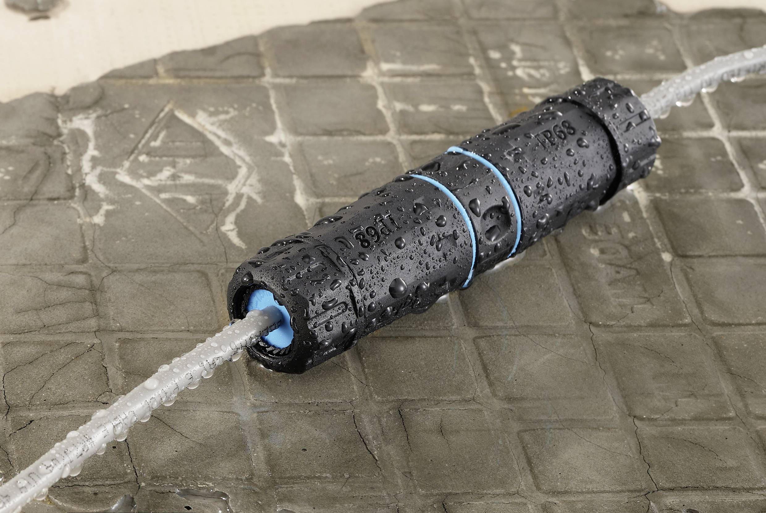 Waterproof cable connector on a wet surface. Two cables connected through the black plug, with blue sealing rings.