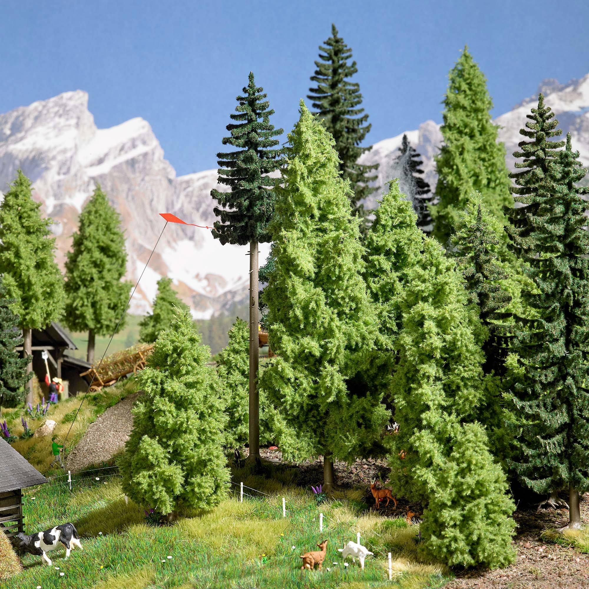An idyllic landscape model featuring tall pine trees, mountains in the background, green meadows and a small farmhouse with animals.