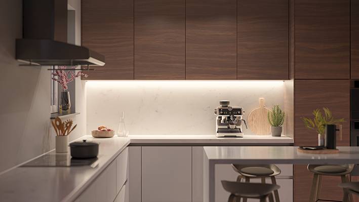 Modern kitchen with wooden cupboards, a coffee machine on the worktop and bright lighting. A drawer unit and decorative items are visible.