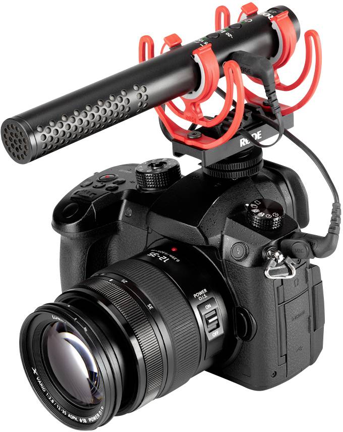 Black digital camera with a large lens and attached black microphone. The camera has red microphone mounts.