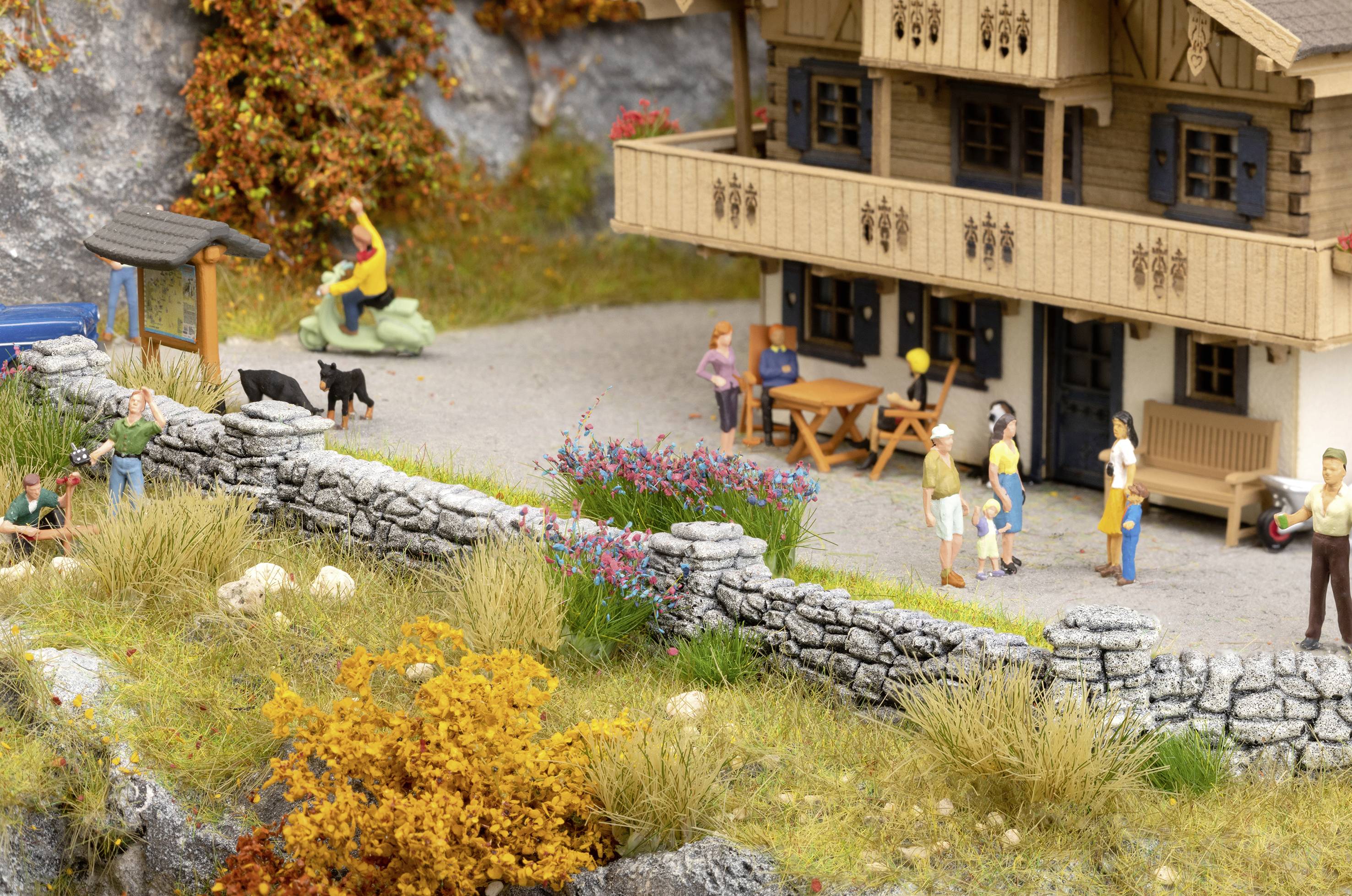 A model depicts a traditional wooden house with figures in the courtyard. Some people are chatting, a child is sitting on a statue, and dogs can be seen.